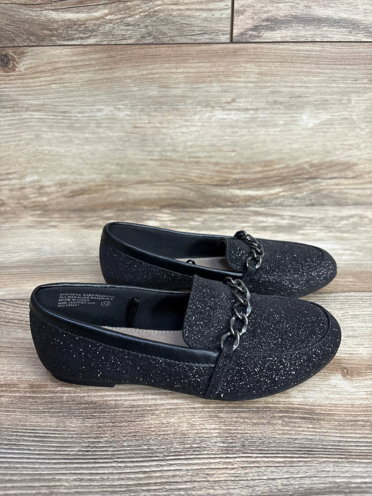 Black glitter loafers with silver chain detail on wooden floor