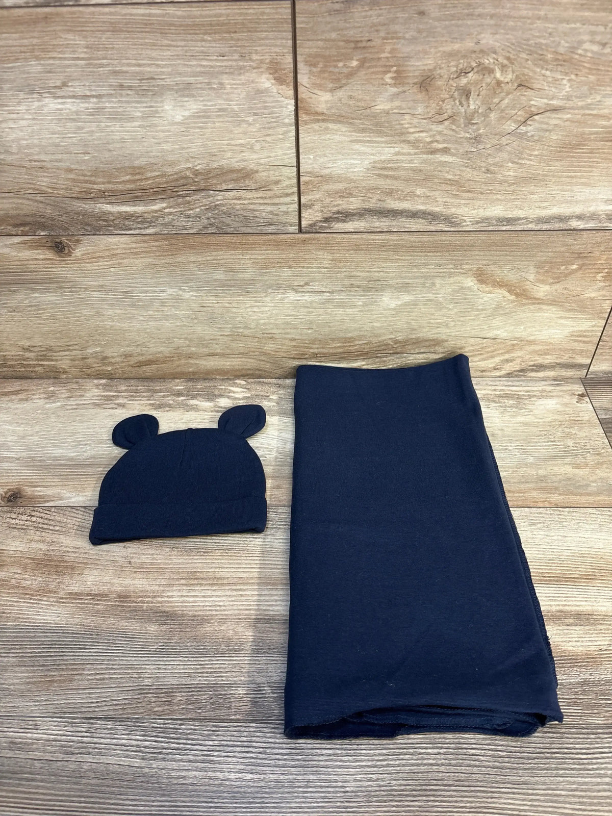 Navy blue baby hat with bear ears and matching blanket on wooden floor