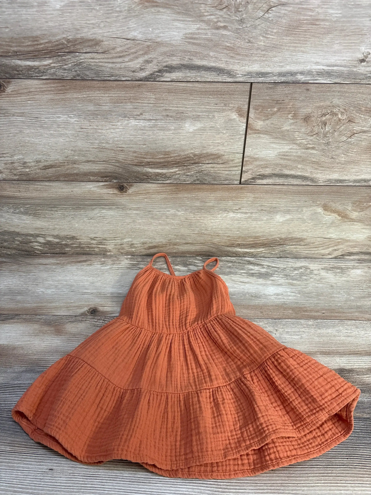 Flat lay of Cat & Jack orange gauze tiered dress with spaghetti straps and crinkled tiers on light wood background