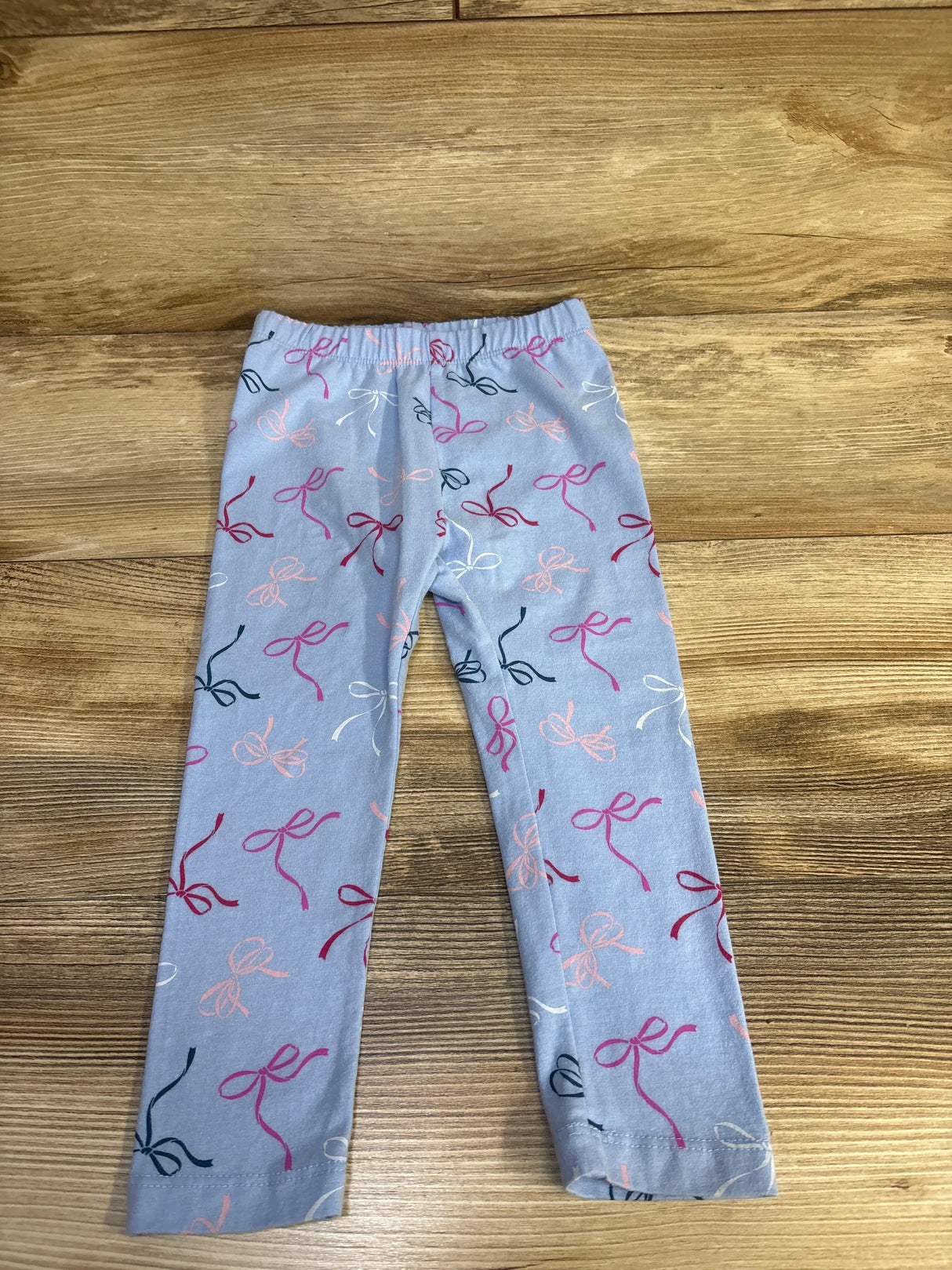 Flat lay of Baby Gap blue leggings size 2T showing pink and navy bow print and elastic waist on wood background