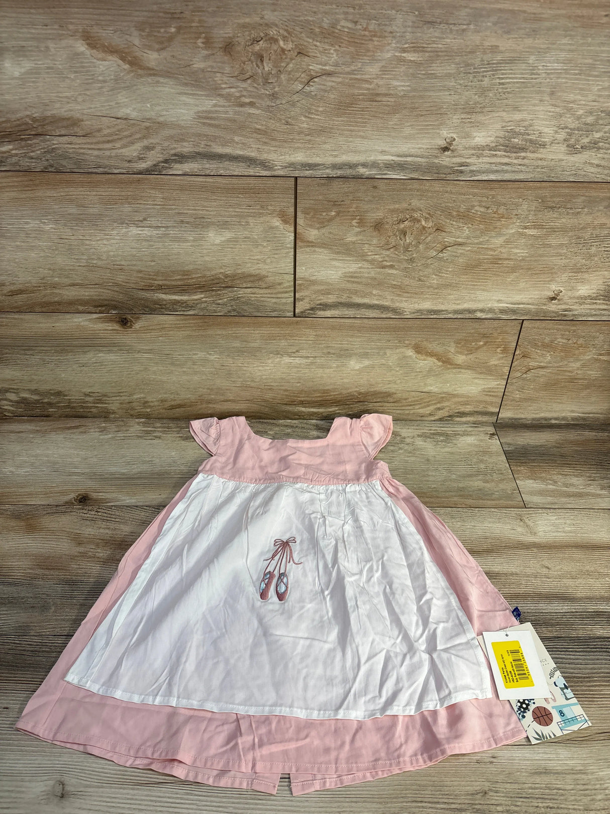 Flat lay of pink Kickee Pants garden dress with white apron and ballet shoe embroidery, size 12-18 months on wood background