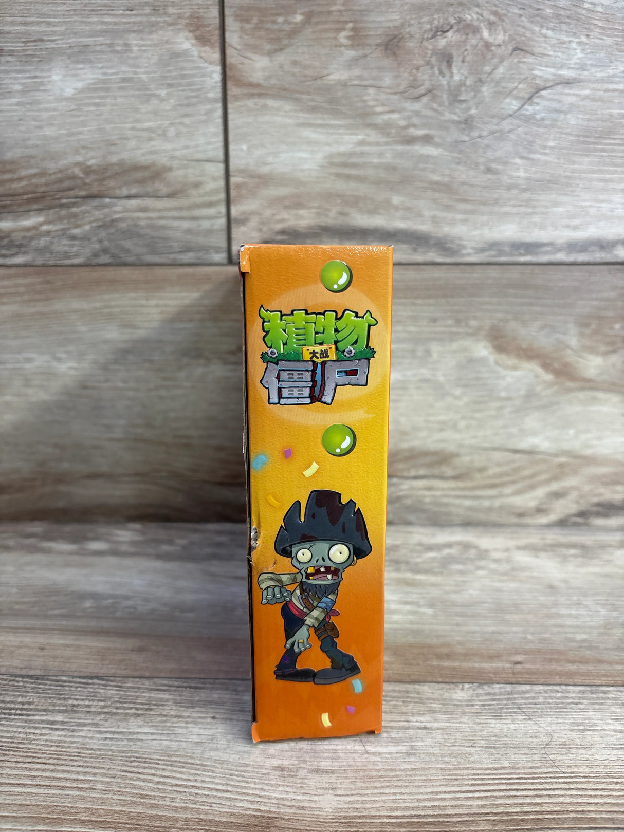 Side view of an orange box featuring a cartoon pirate zombie character and Chinese text, against a wood background