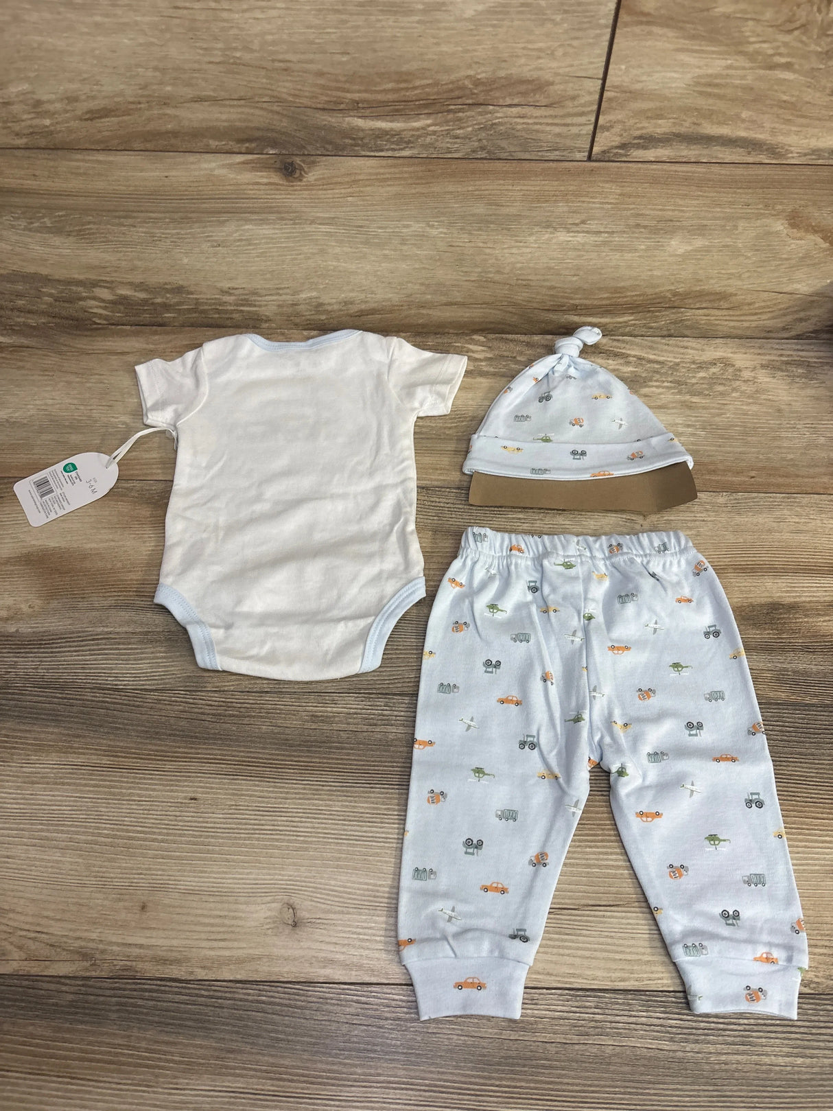 Baby outfit set with white onesie, light blue pants and hat with colorful vehicle prints on wooden floor