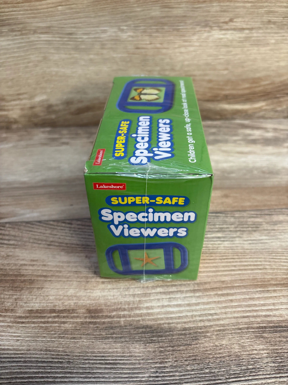 Front and top view of Lakeshore Super-Safe Specimen Viewers box, green packaging with Lakeshore logo, sealed plastic on wood