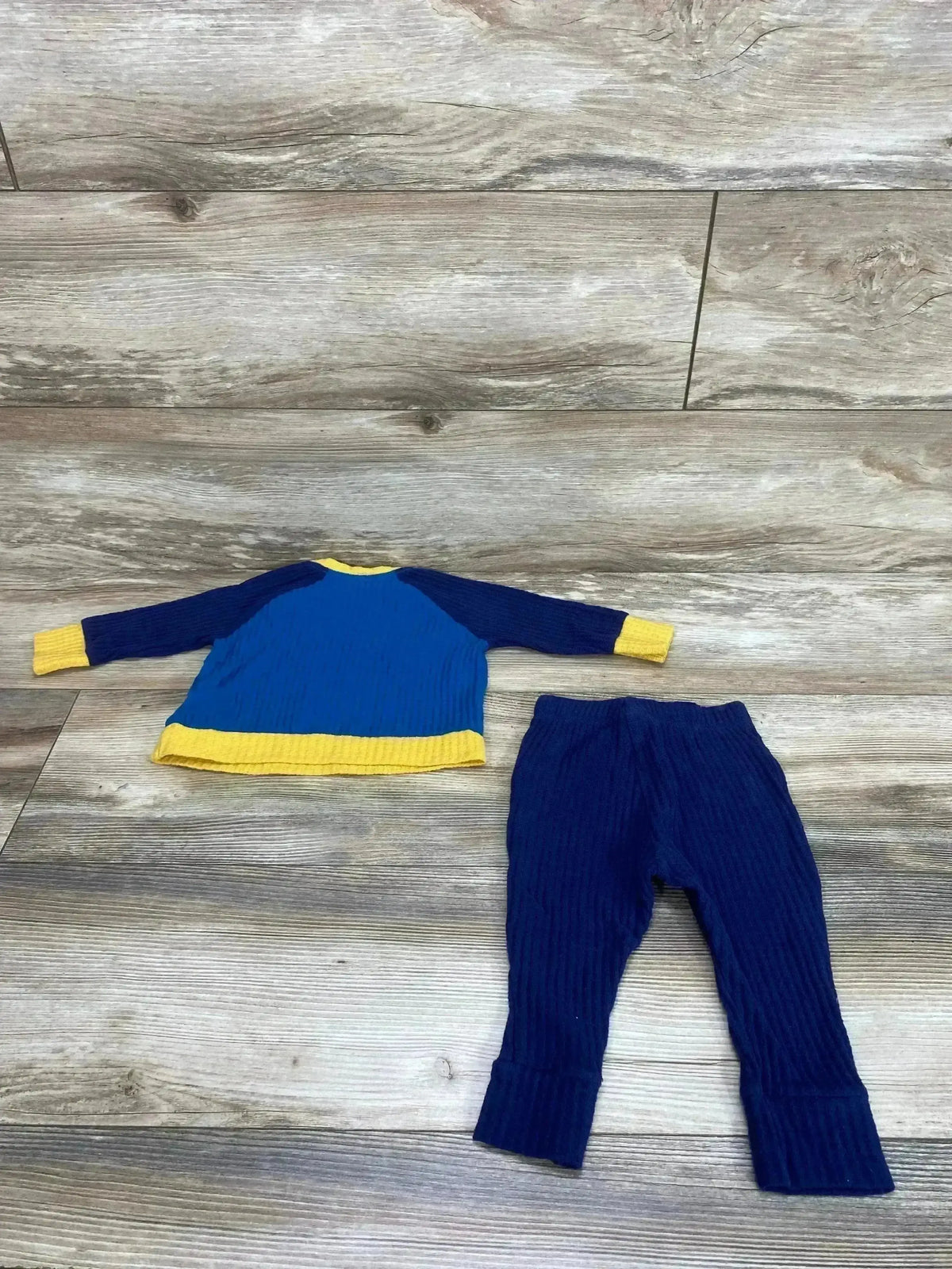 Flat lay of Cat and Jack waffle knit baby set, navy top with yellow trim and ribbed navy pants on wood floor