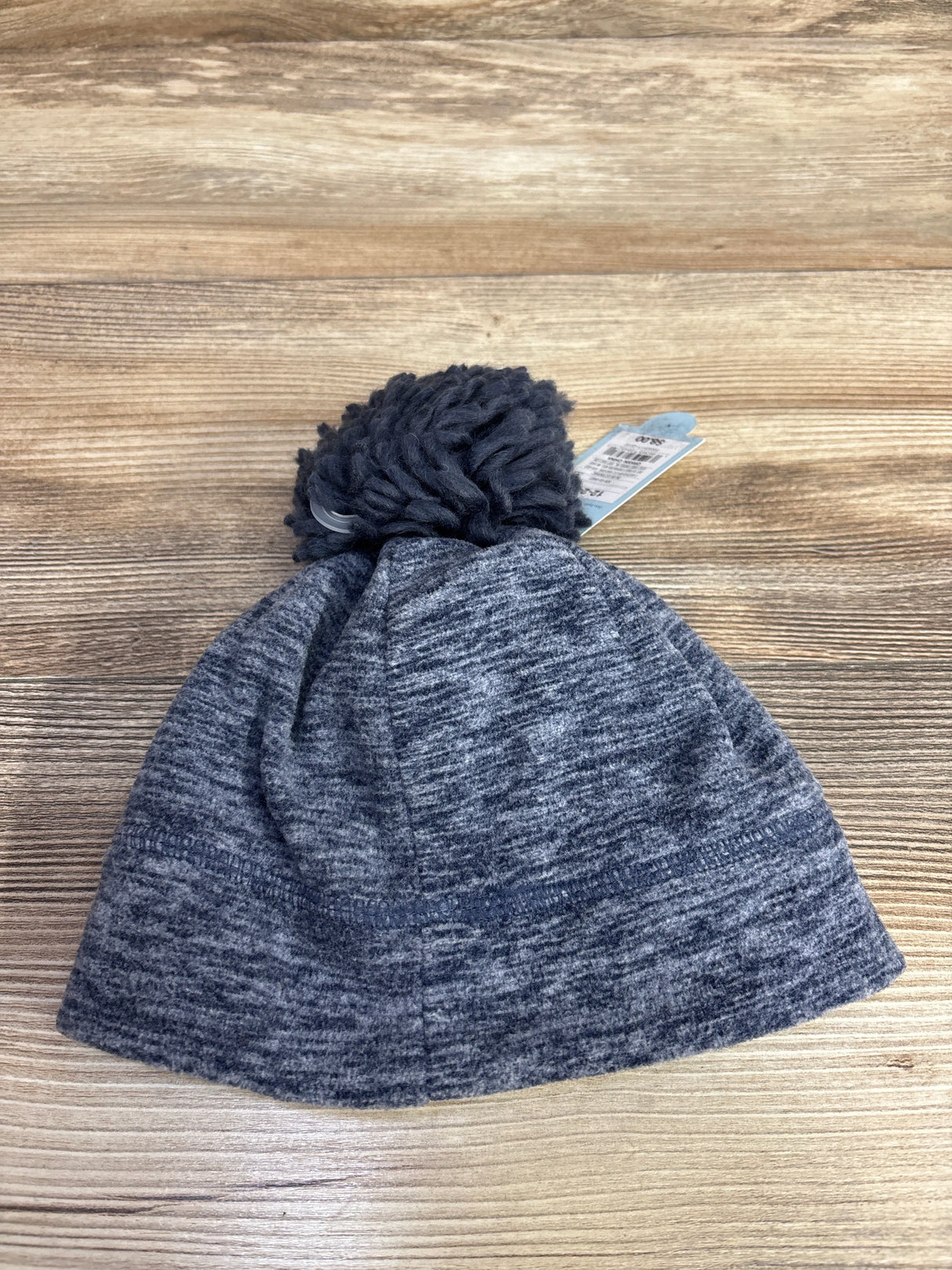 Grey knit winter beanie hat with pom-pom on wooden surface