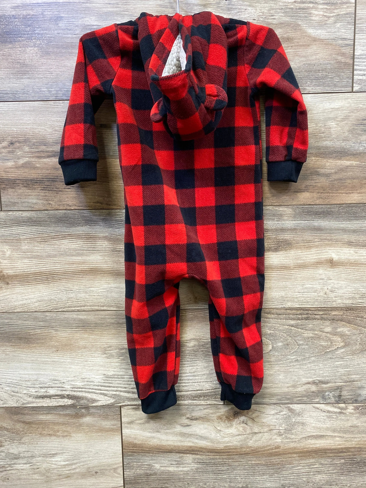 Red and black buffalo plaid fleece baby onesie with hood shaped like a bear, on wooden floor