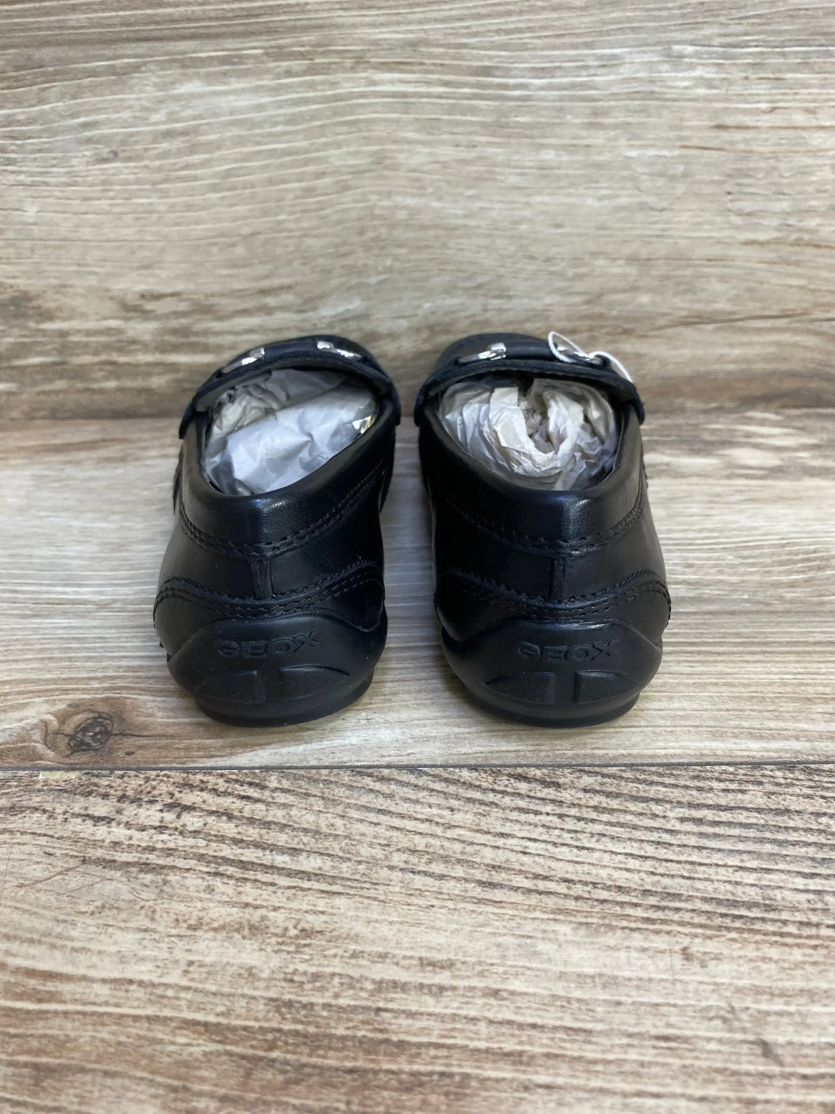 Rear view of GEOX black chain loafers size 10C showing heel logo, chain detail and rubber soles on wood background