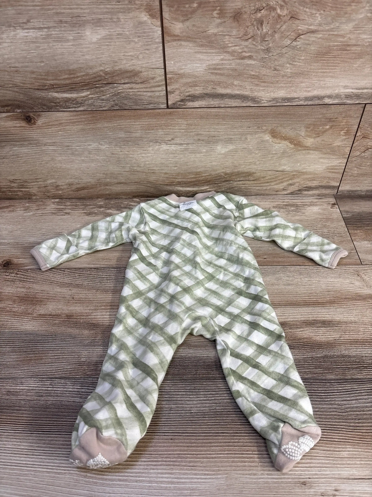 Front view of Burt’s Bees Baby Organic Sleeper in green and white plaid, showcasing long sleeves and covered feet with a wood-look background