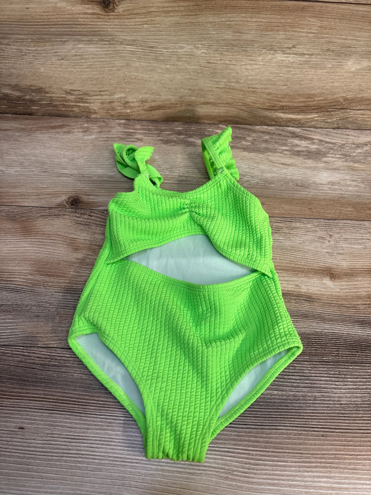 Front view of Shein green textured cut-out swimsuit with tie shoulder straps on a wood-grain background