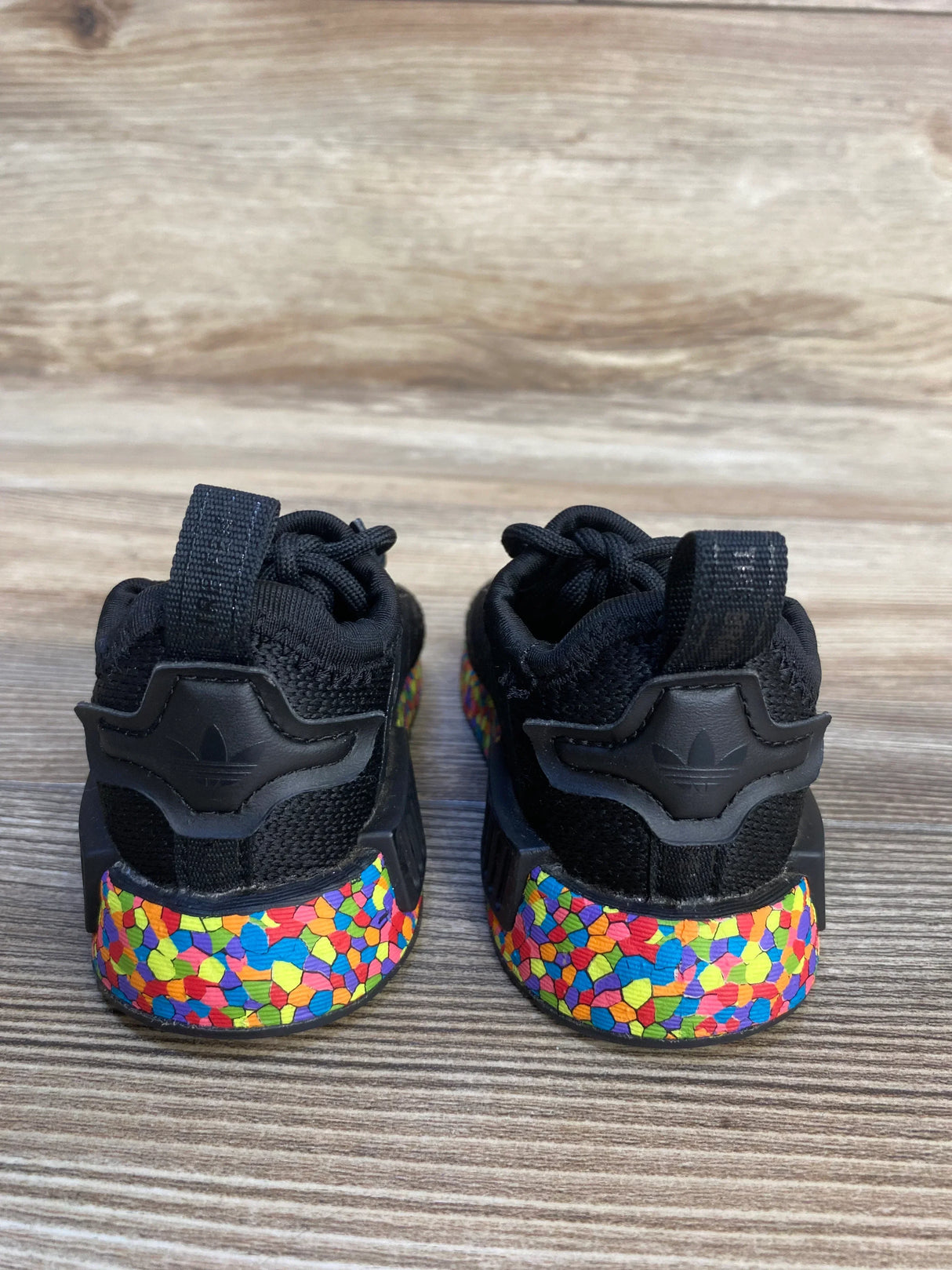 Black kids sneakers with multicolor mosaic soles on wood background, rear view