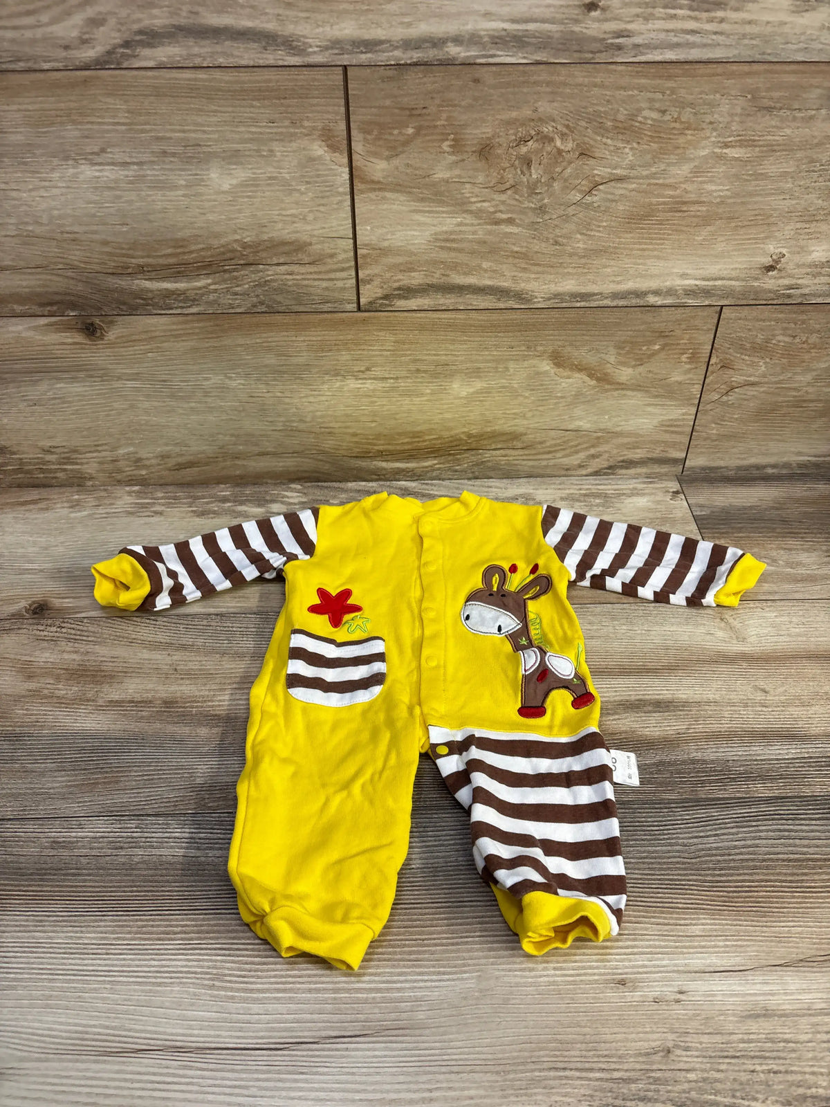 Front view of yellow snap baby giraffe coverall with embroidered giraffe, brown-and-white striped sleeves and leg, and front pocket on wood floor