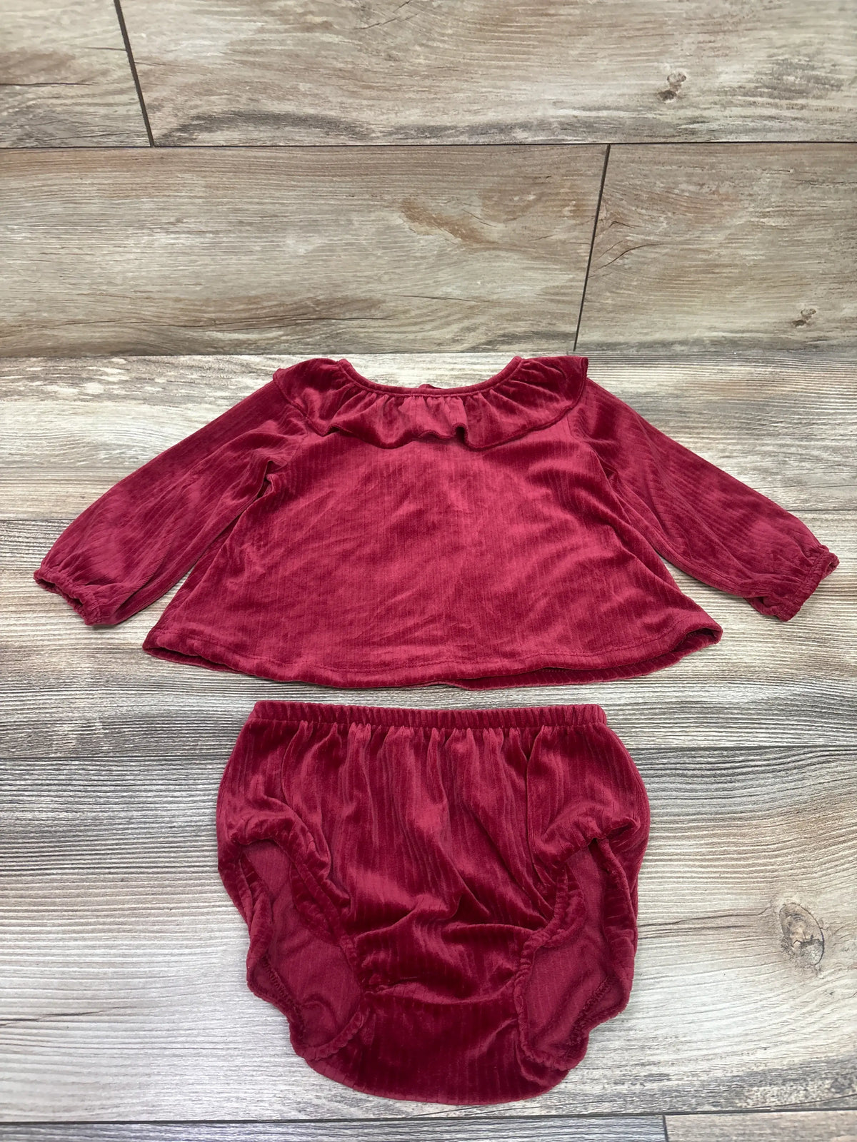 Top-down view of a red velvet shirt and bloomers set showcasing a ruffled collar and elasticized bloomers on a wood-look floor