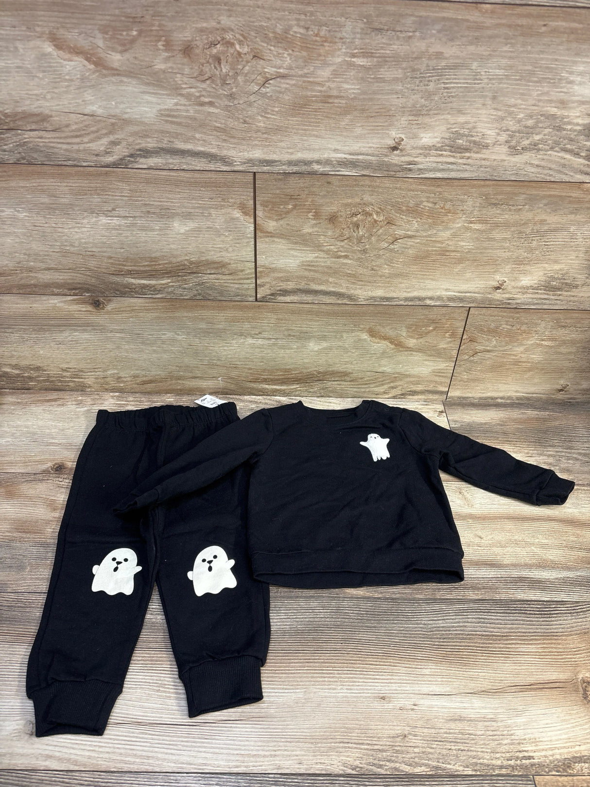 Front-flat view of Cat & Jack black toddler sweatshirt and joggers set showing white ghost graphics on chest and knees on wood floor background