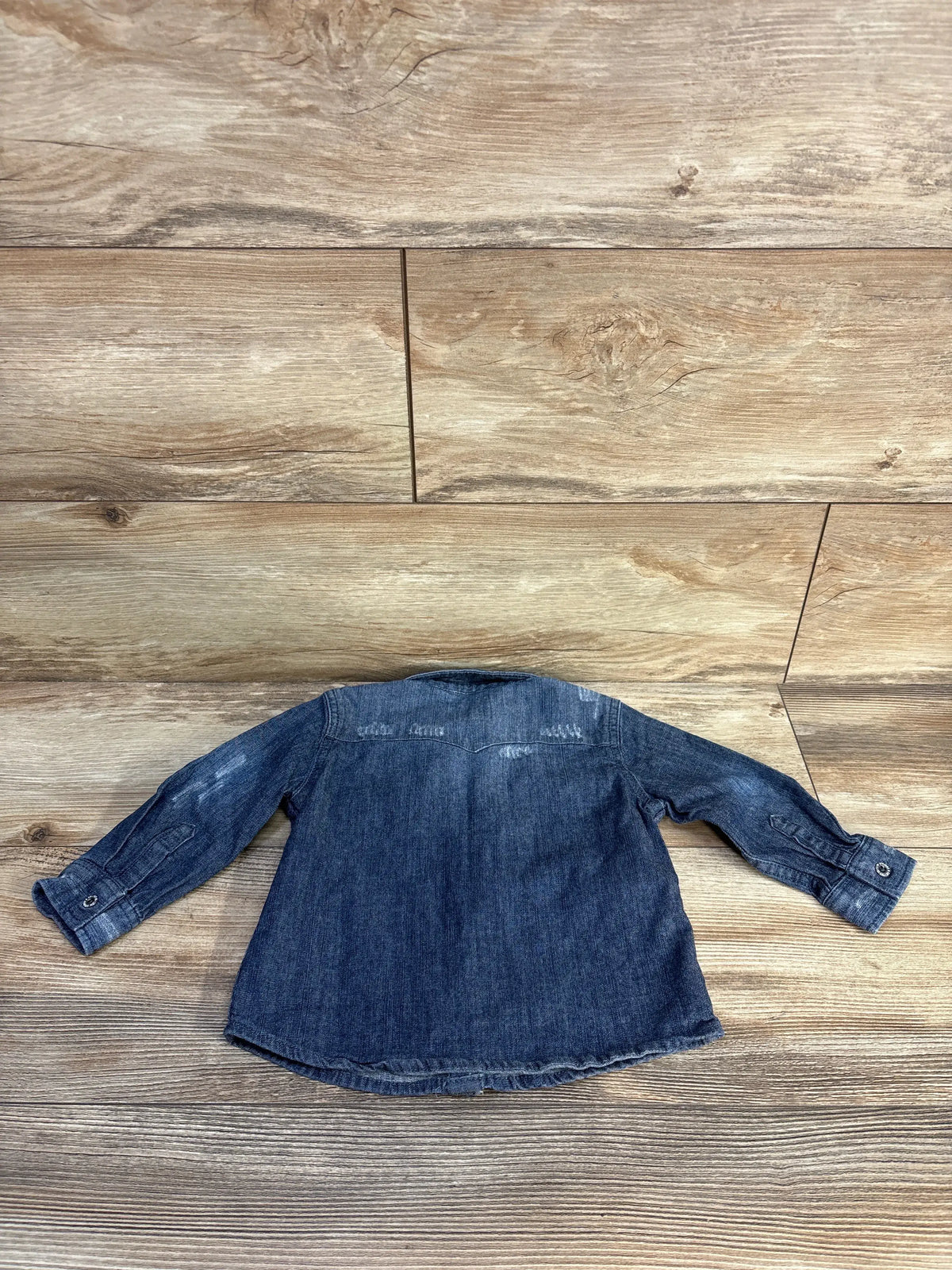 Back view of Levi’s blue chambray button-up shirt showcasing long sleeves and button cuffs with wood-look floor background