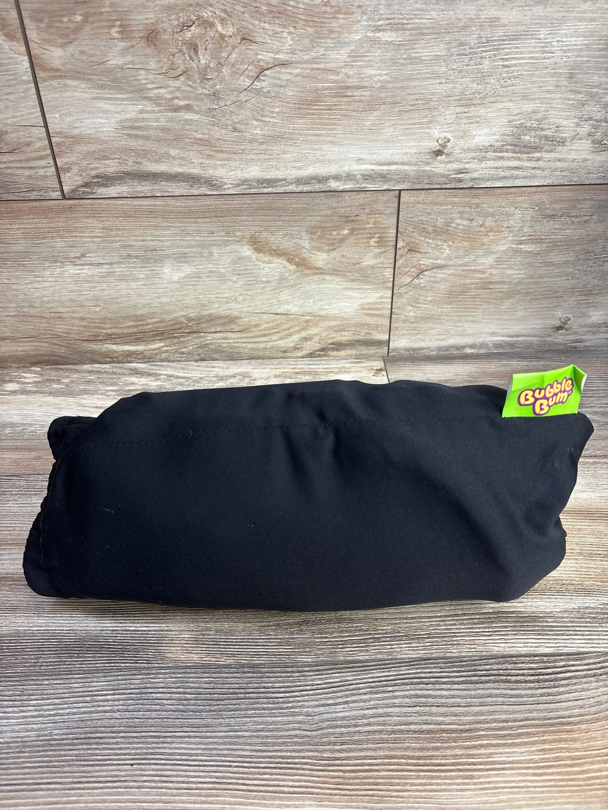 BubbleBum inflatable booster seat in black storage pouch, compact folded on wood-grain surface