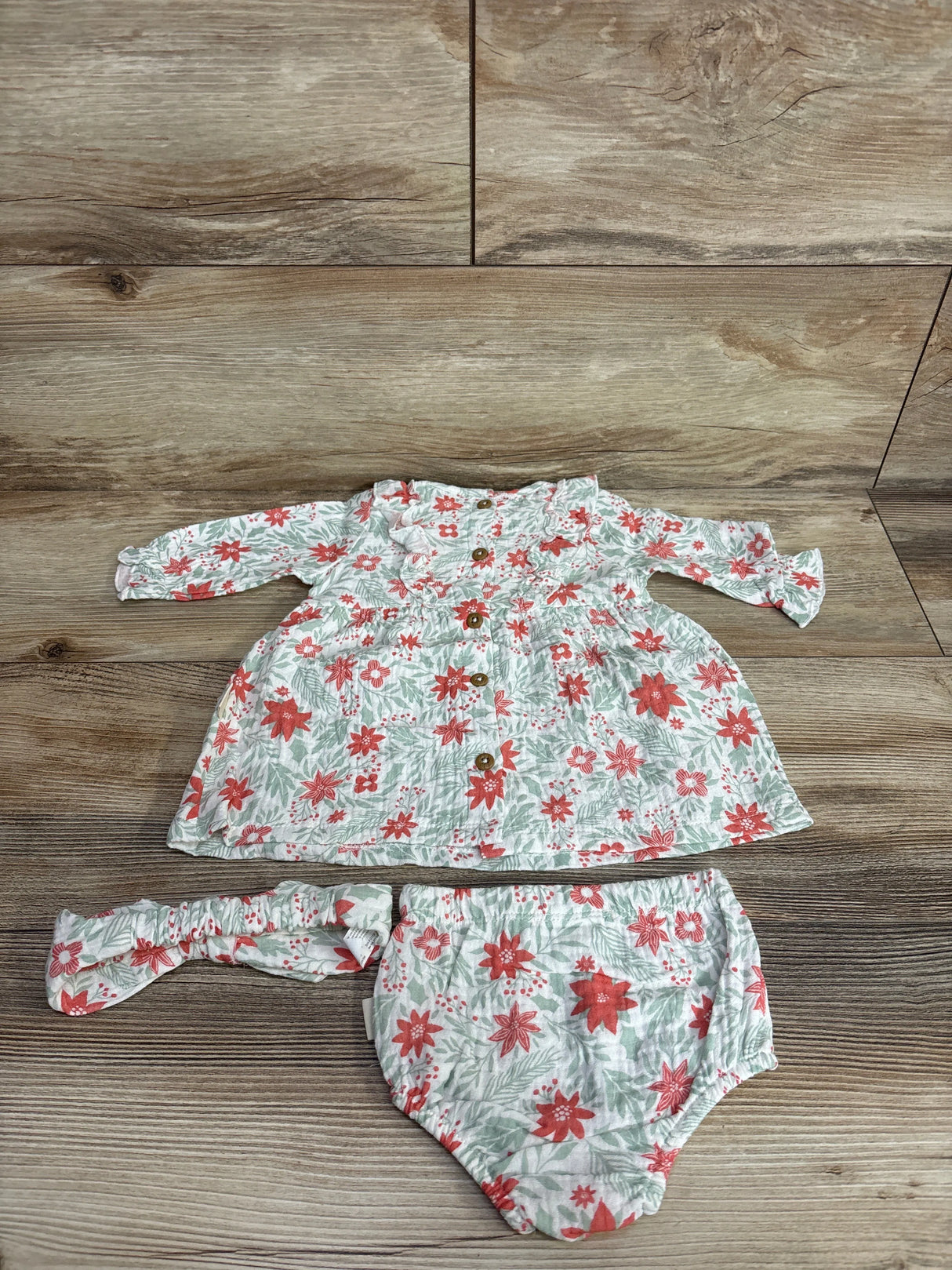 Flat lay of Rabbit Bear 3-piece newborn dress and headpiece set showcasing ruffle collar, wooden buttons, and coral floral print on wood background
