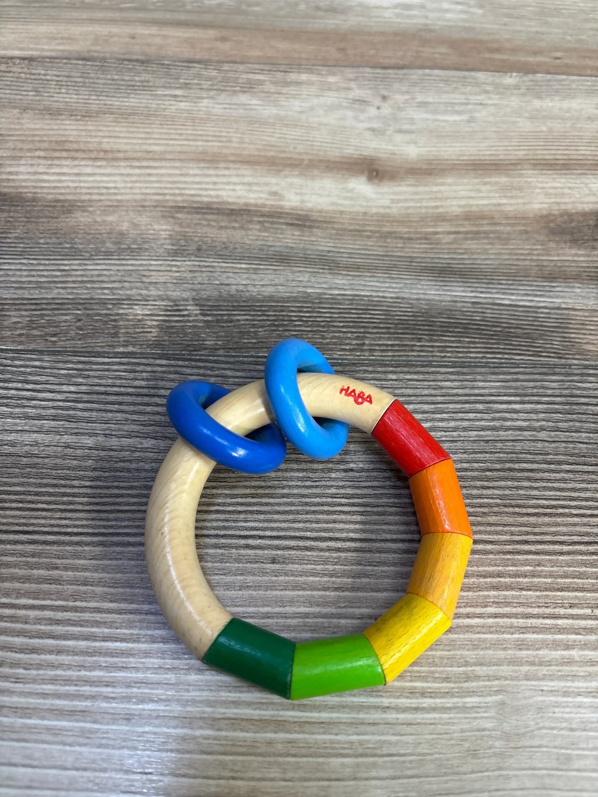 Top view of HABA Kringelring wooden clutching toy showcasing rainbow-colored beechwood beads on a wood-grain background