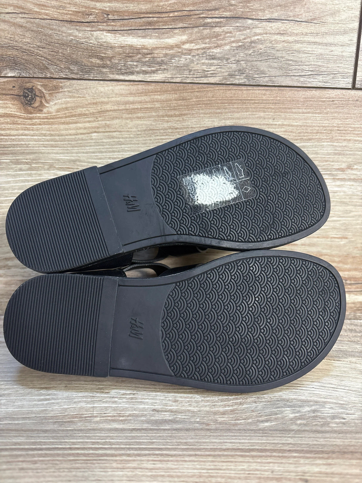 Pair of black rubber-soled kids shoes with patterned treads on wood floor