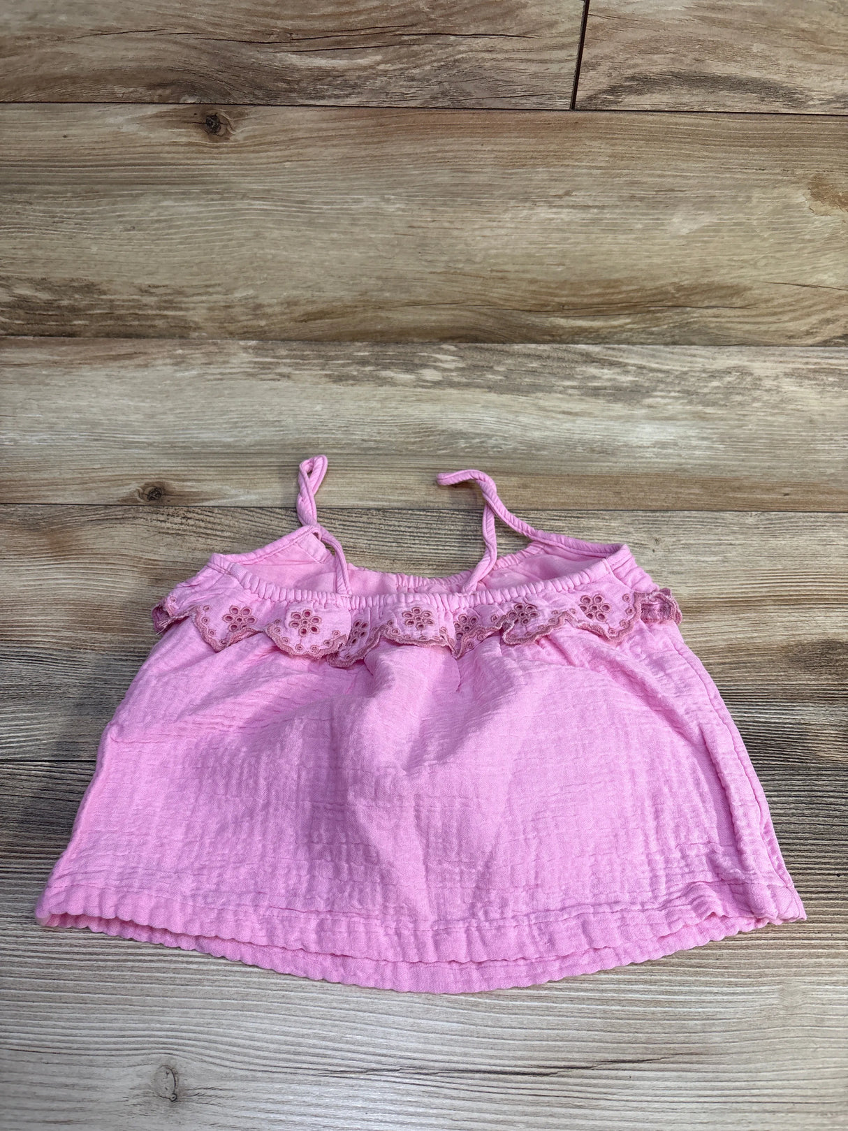 Flat lay of Gymboree pink eyelet gauze tank top size 2T showing ruffled eyelet trim on wood background