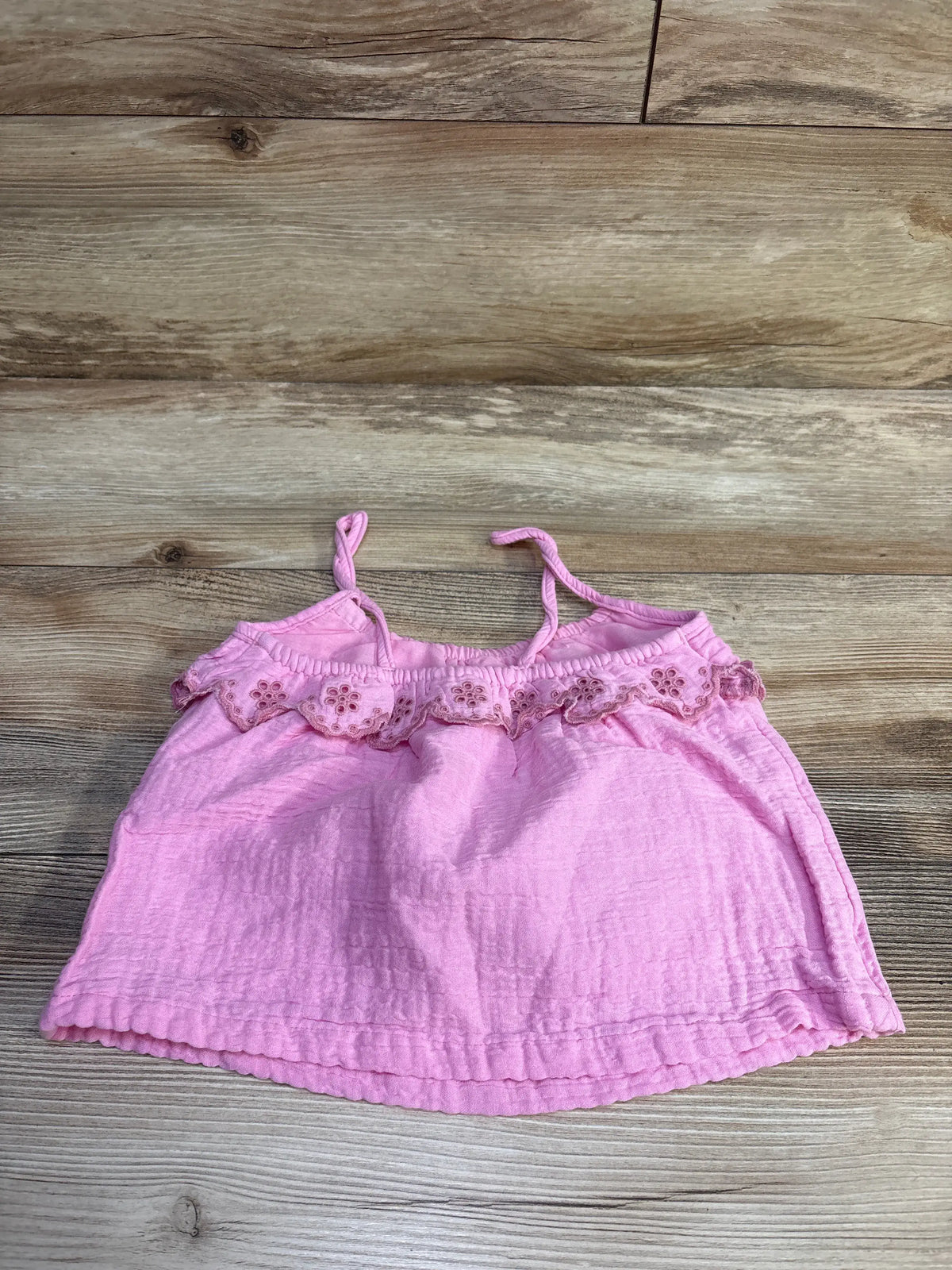 Flat lay of Gymboree pink eyelet gauze tank top size 2T showing ruffled eyelet trim on wood background