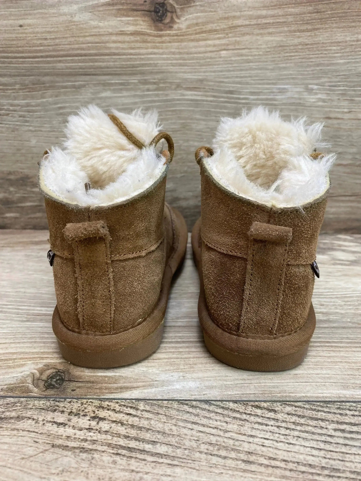 Rear view of Lamo Chukka toddler boots showing chestnut suede exterior, cream faux-fur lining, and pull tabs on wood floor