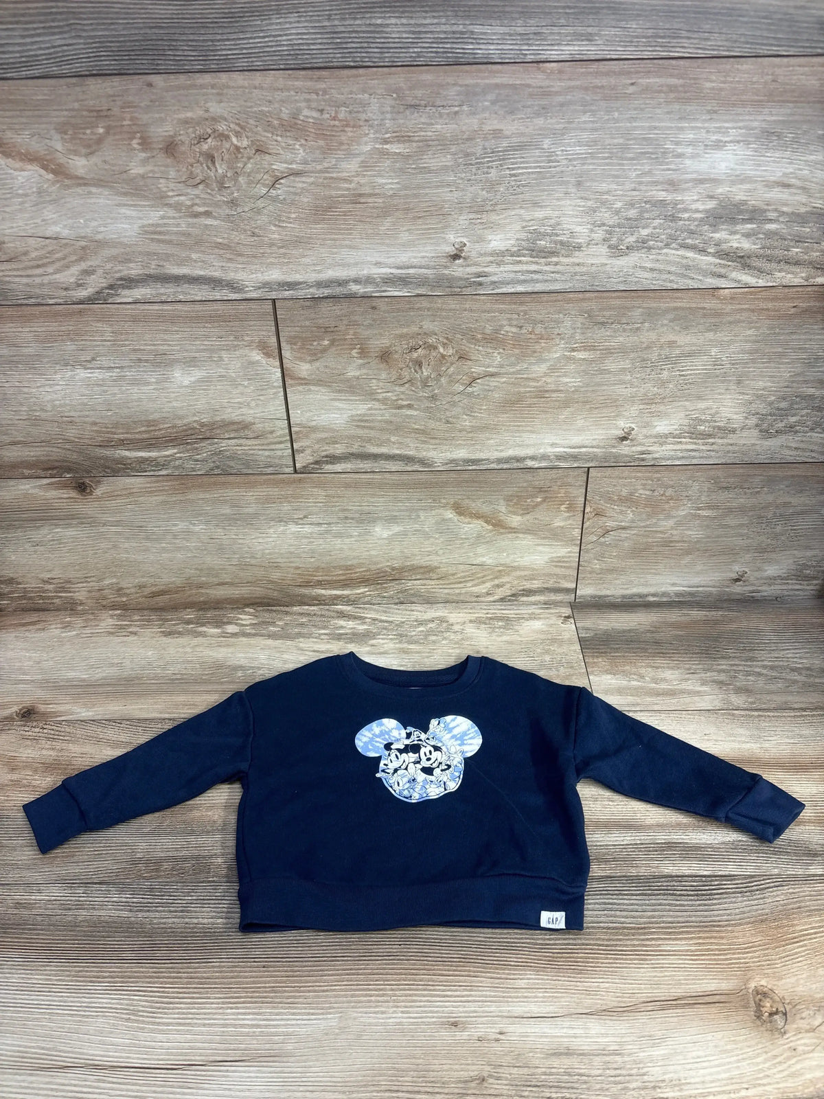 Navy blue toddler sweatshirt with cartoon mouse graphic, long sleeves, laid on wood floor