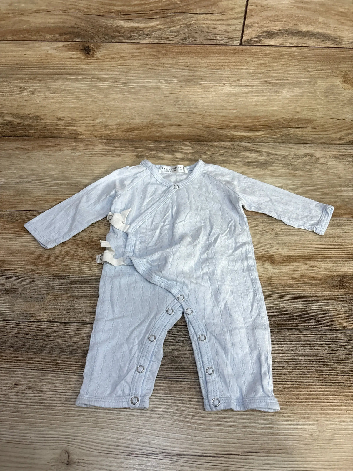 Light blue baby romper with long sleeves and snap buttons on wooden background