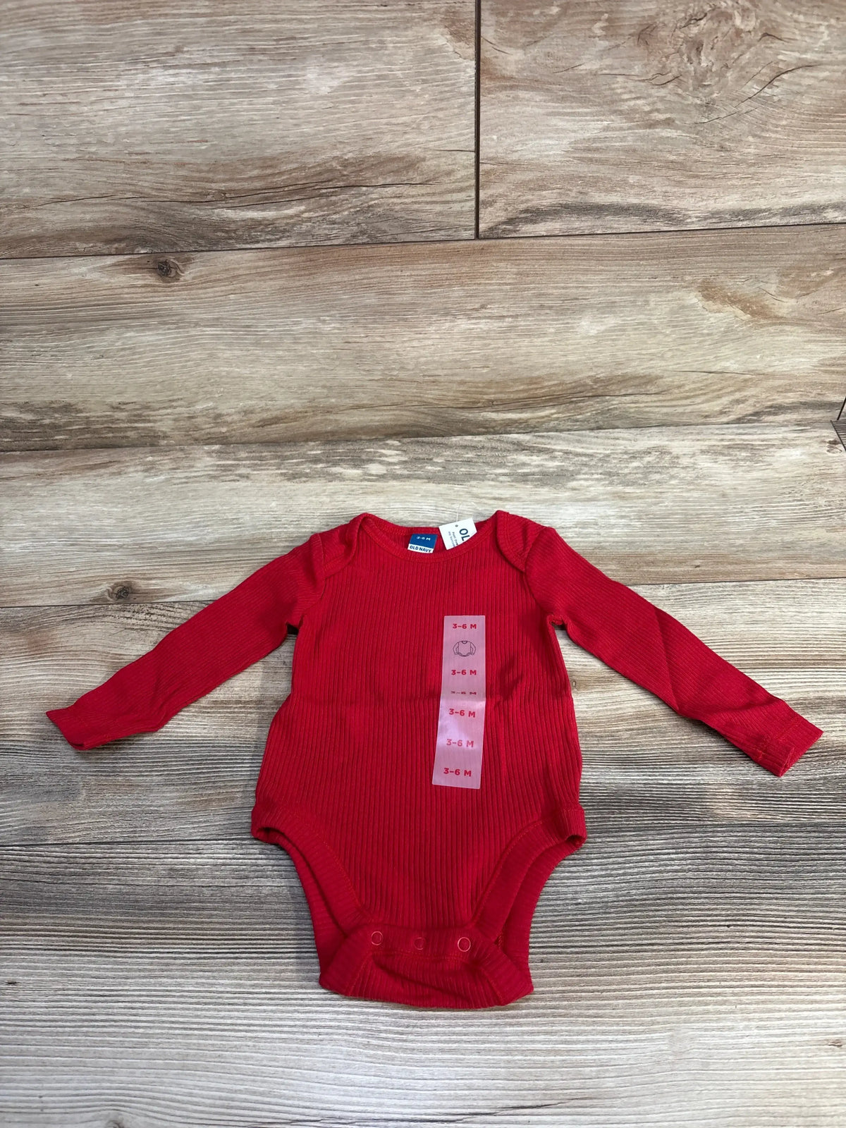 Red ribbed baby bodysuit with long sleeves, size 3-6 months, on wood floor
