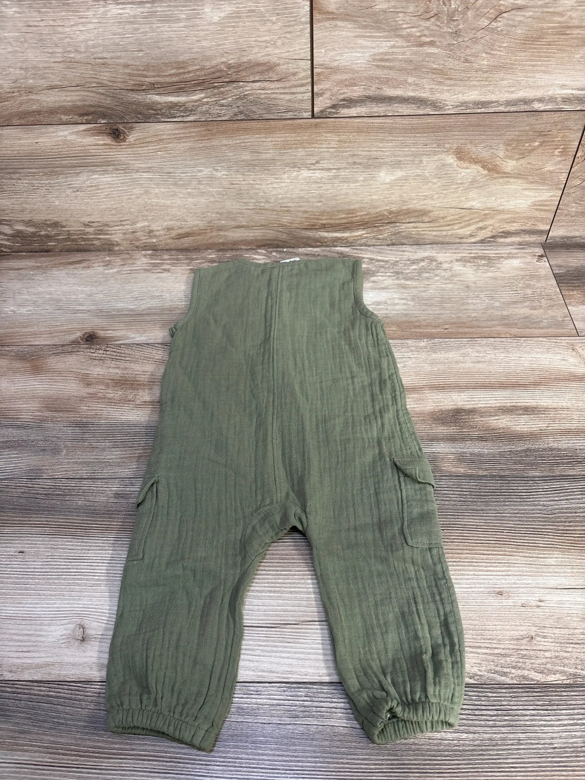 Flat lay of Old Navy sleeveless pocket jumpsuit showcasing side pockets, elastic ankles, and textured green fabric on wood floor background