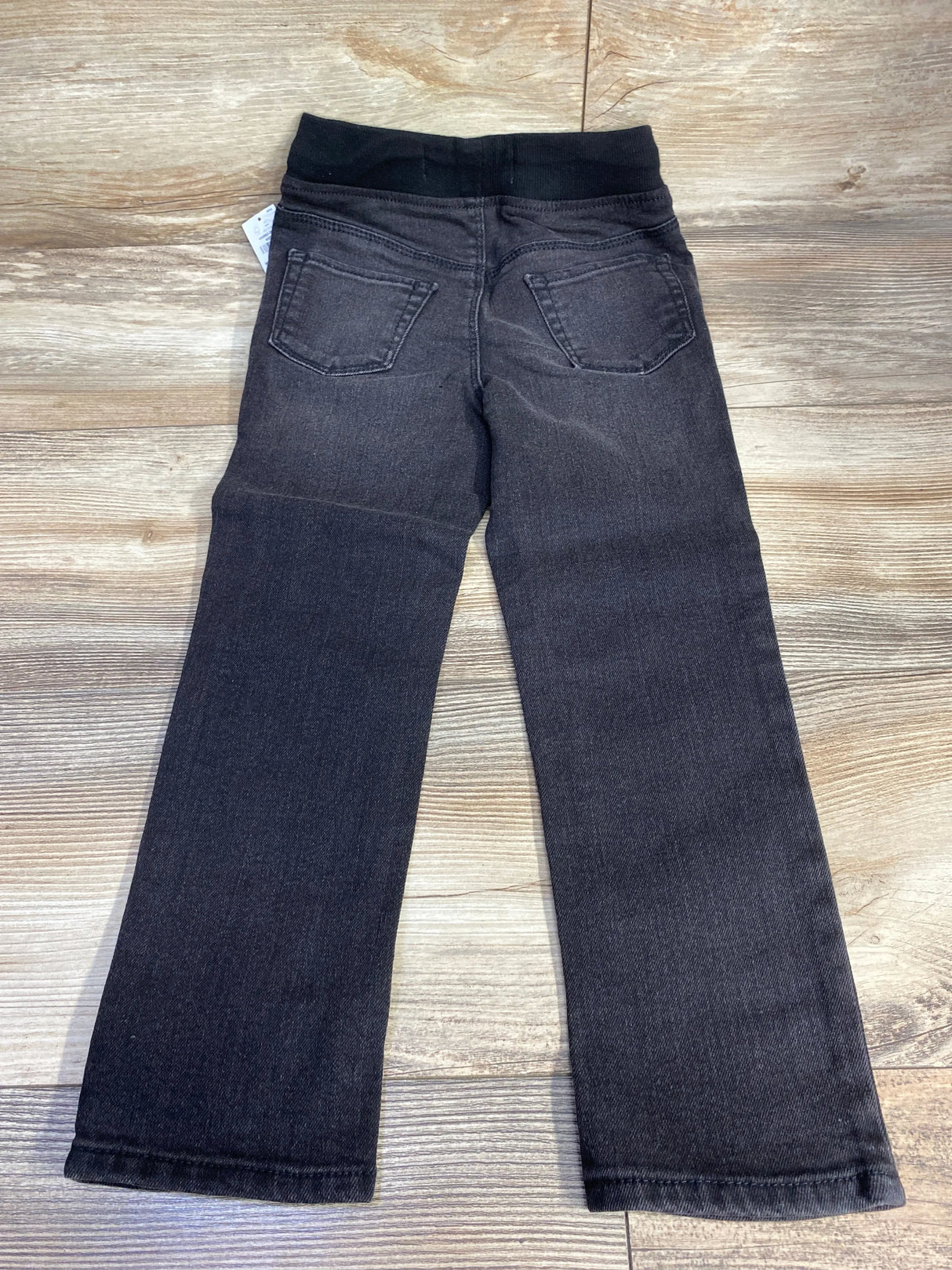 Children's black pull-on jeans with elastic waistband and back pockets on wood floor