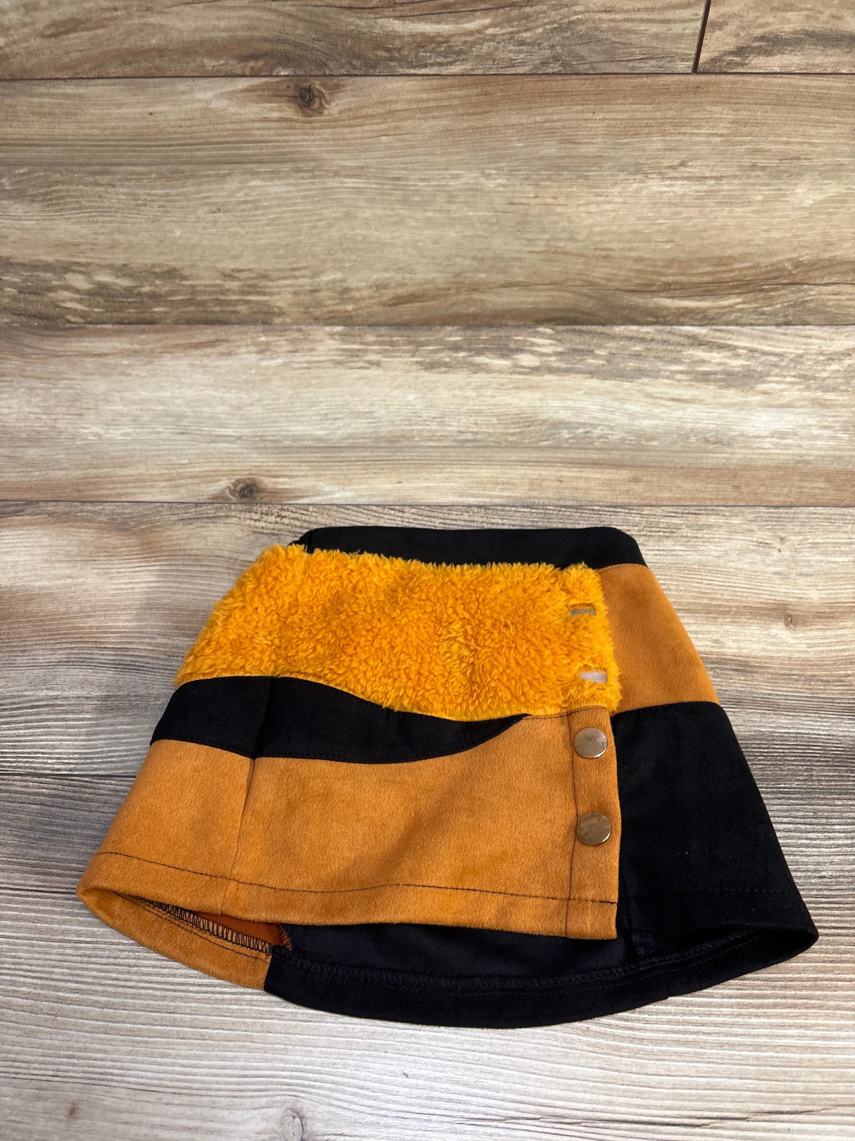 Flat lay of toddler faux-fur skirt in black and orange showing plush orange panel and side snap buttons on wood background
