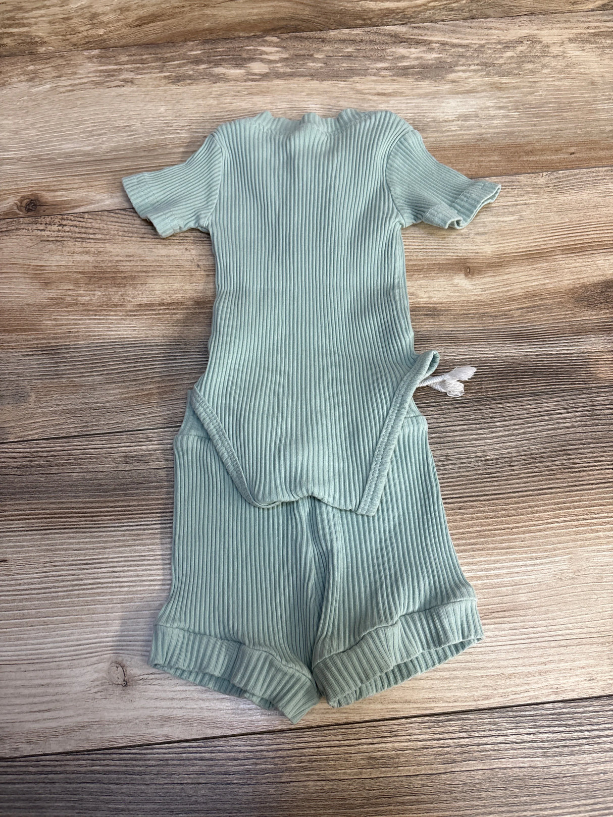 Light green ribbed baby romper with short sleeves and shorts on wood background