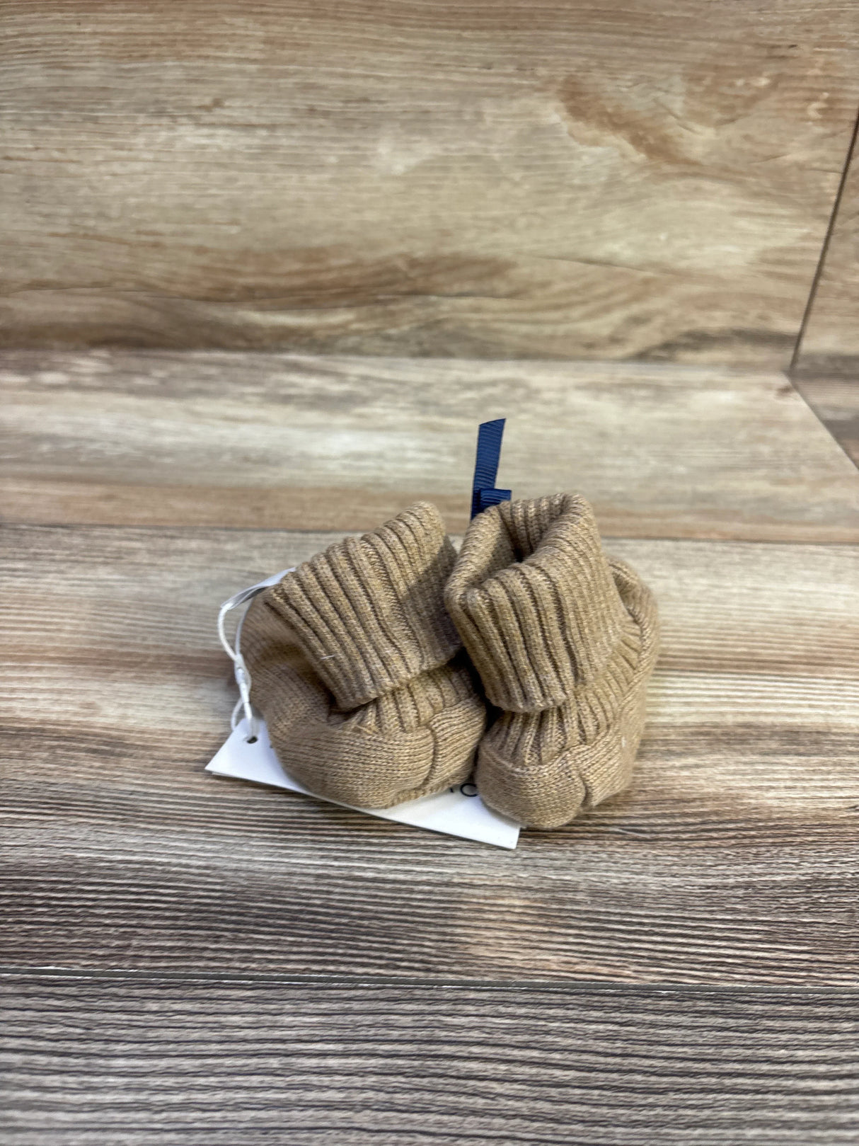 Front view of brown knit baby sweater booties showcasing ribbed fold-over cuffs and knit texture on a wood tabletop