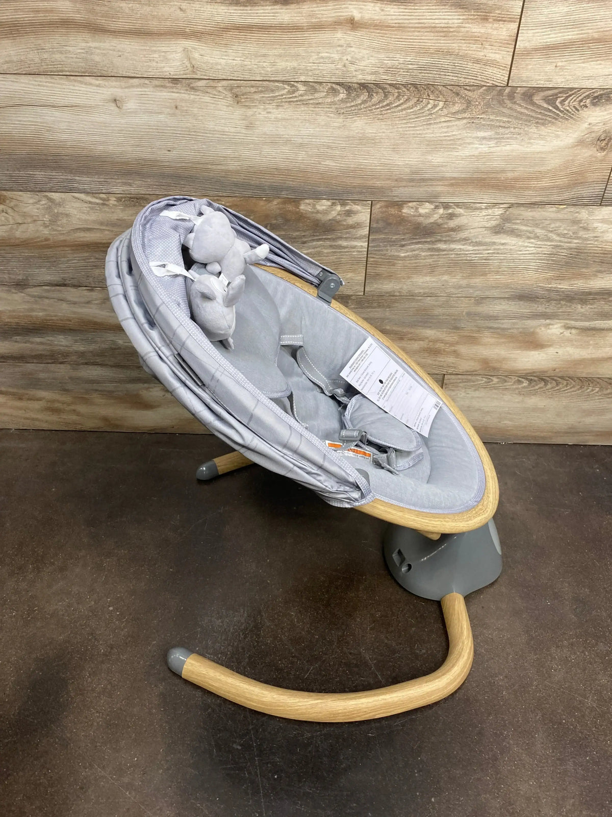 Angled view of Safety 1st Bluetooth baby swing in gray showing wooden rocker frame, padded seat with harness and plush toys