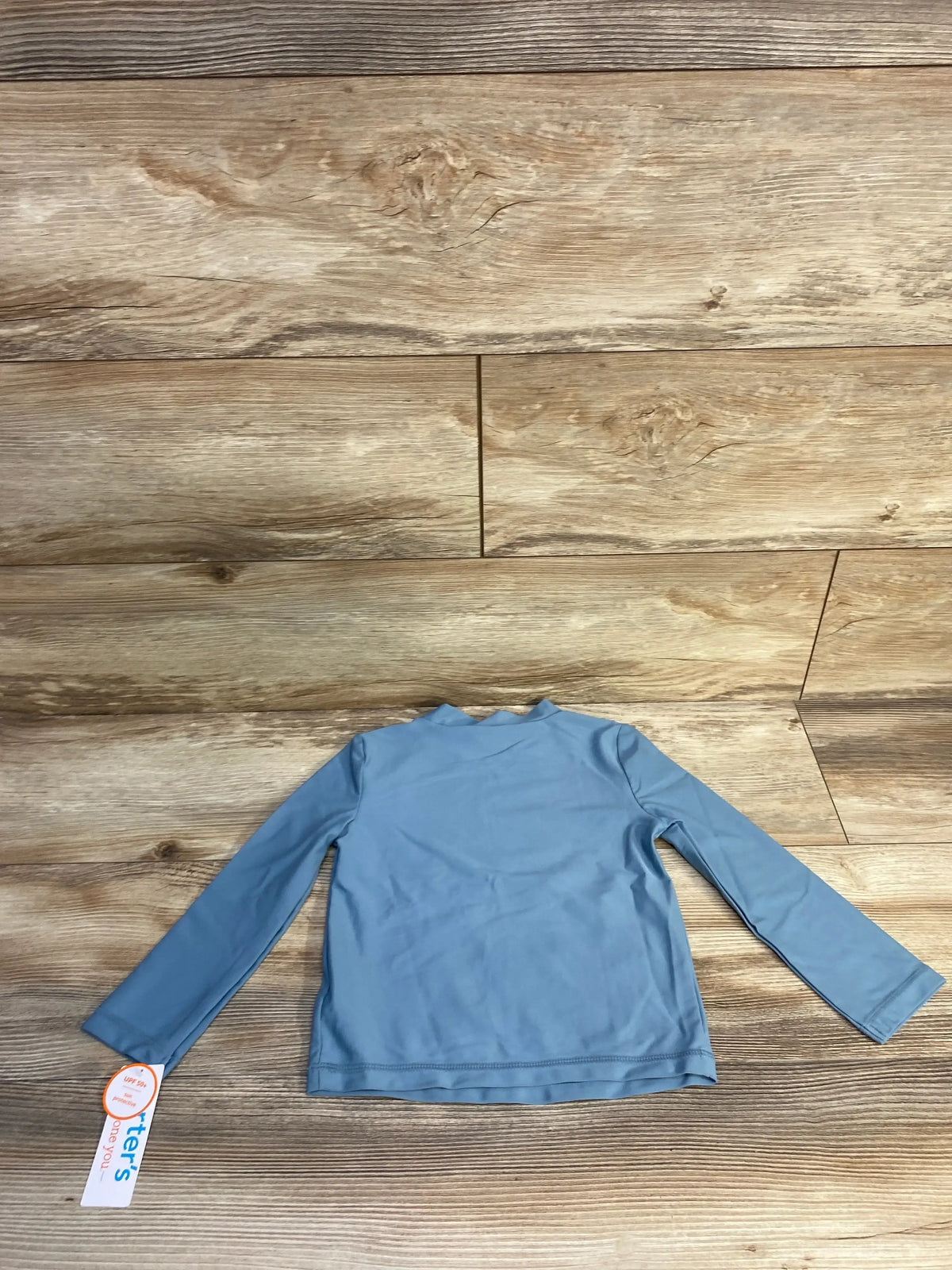 Back view of blue toddler long-sleeve rash guard showing crew neckline and long sleeves on wood plank background