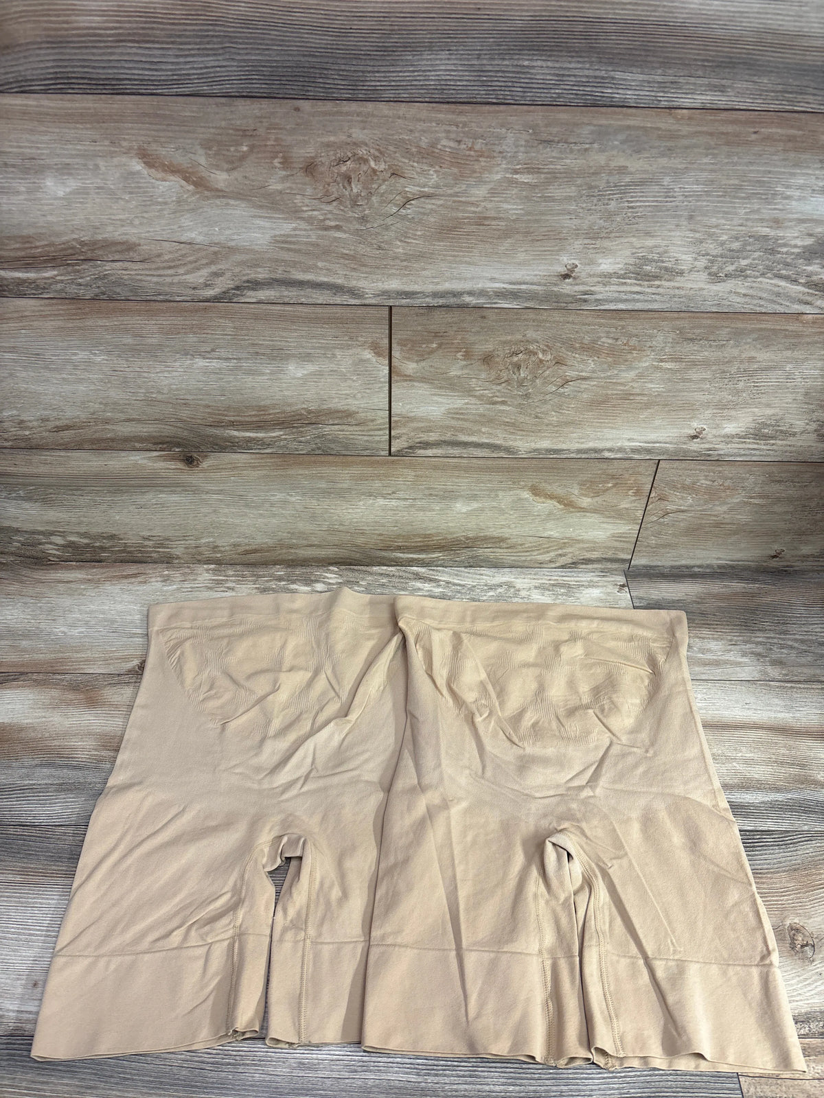 Top view of beige seamless maternity shapewear shorts showcasing the high waist and longer legs on a wood-look floor