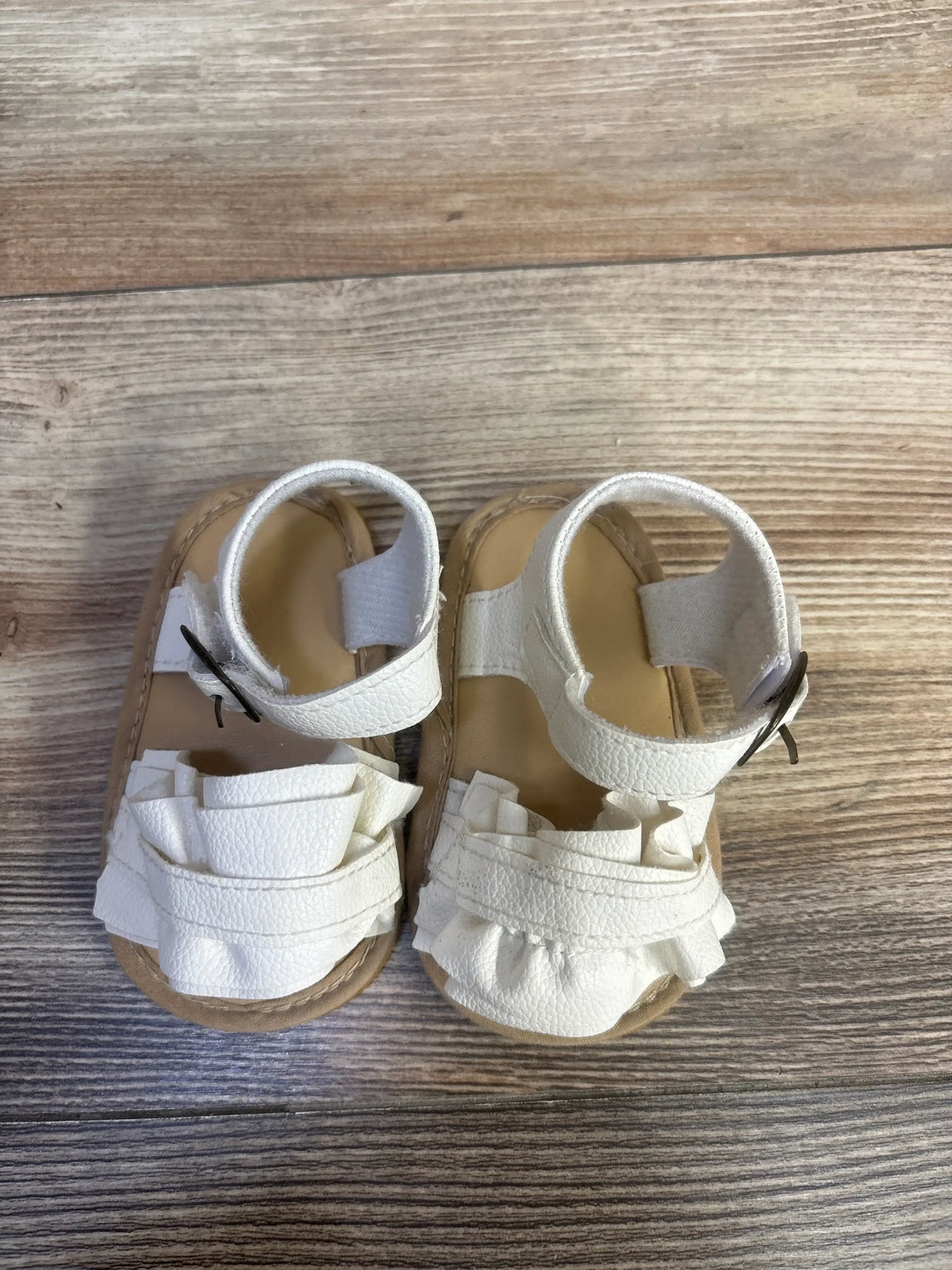 Top view of white Muchenggift bowknot soft sole sandals, size 2C, showcasing bowknot details and ankle straps on wood