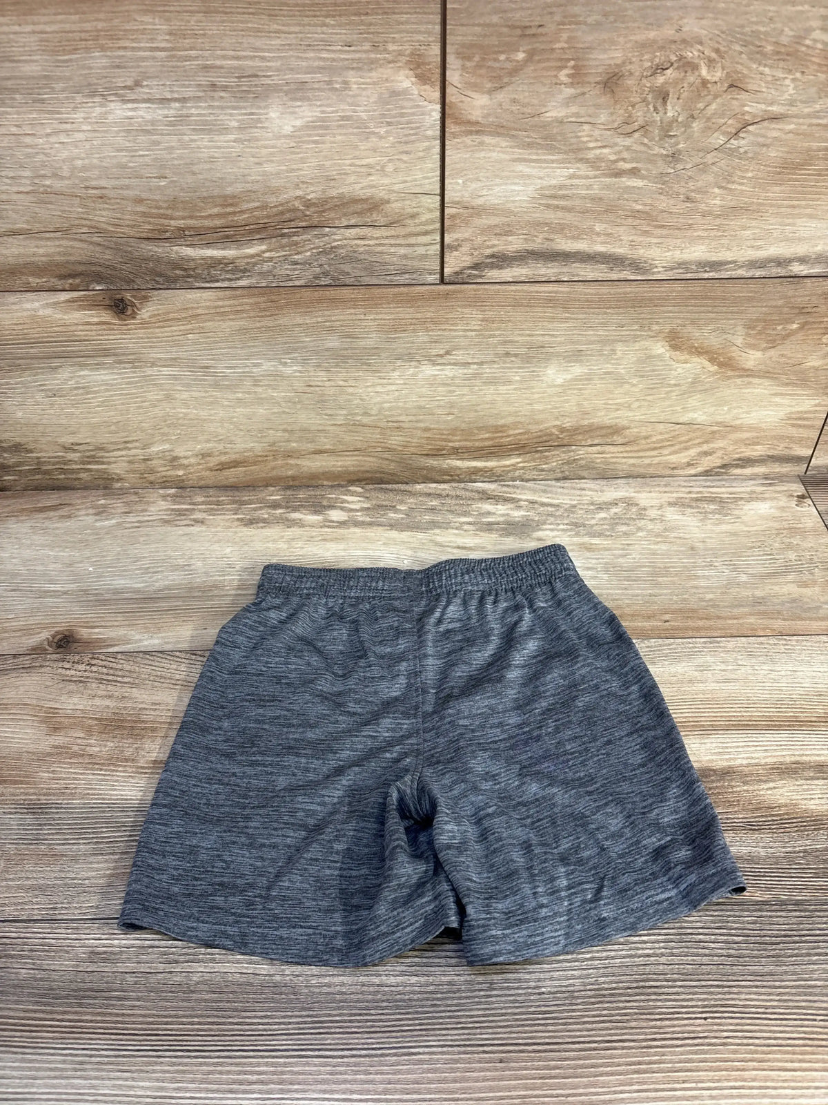 Flat lay of toddler grey Under Armour athletic shorts showing elastic waistband and heathered fabric on wood floor background