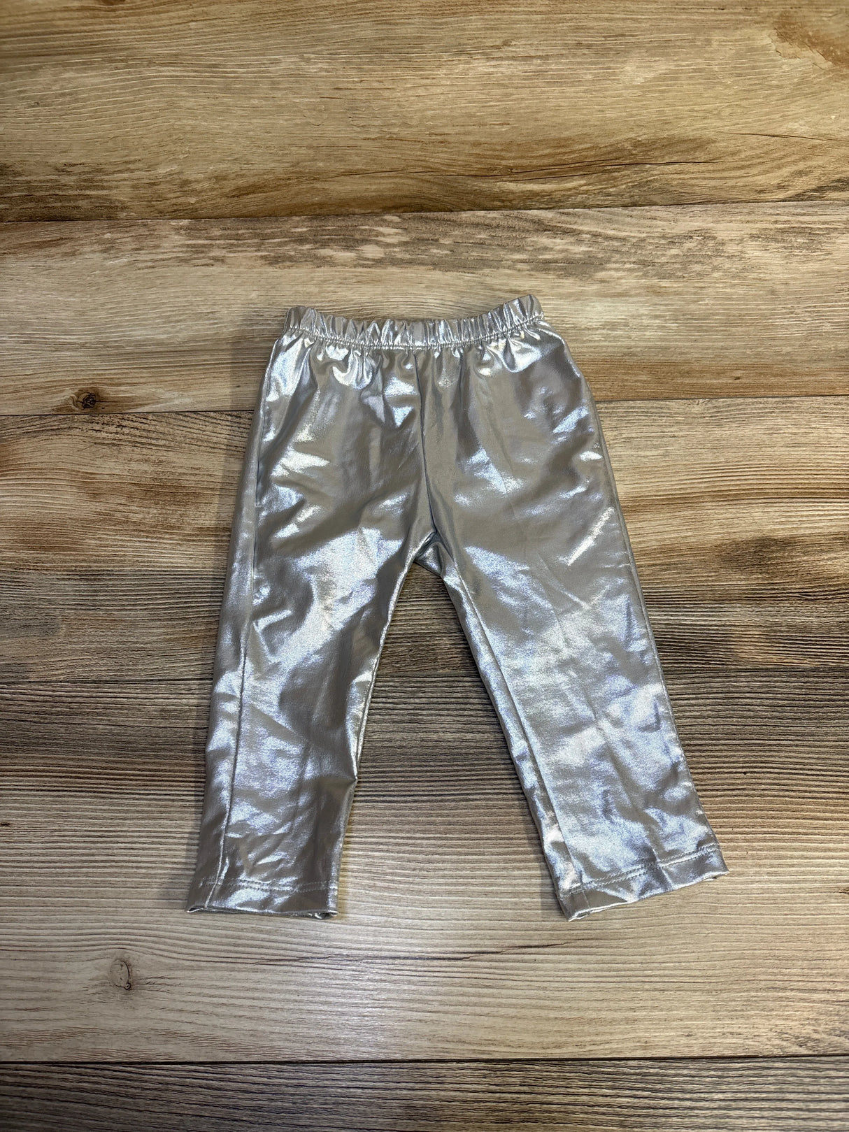 Silver metallic toddler leggings with elastic waistband on wooden floor background