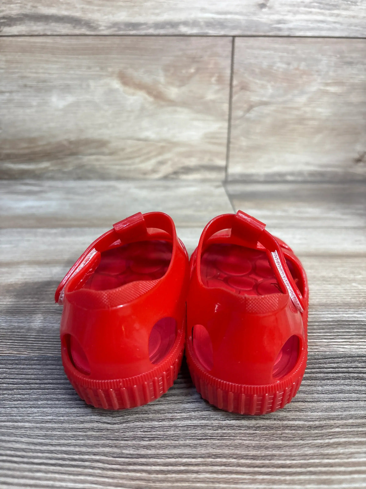 Close-up of red jelly fisherman sandals showcasing hook and loop closures on a wood-look surface