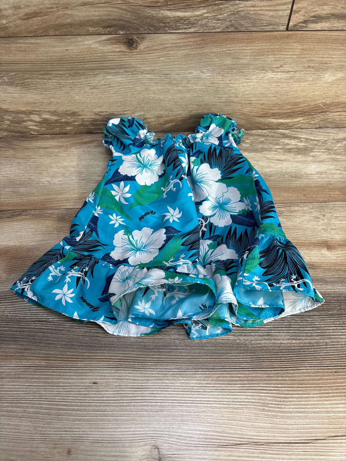 Top-down view of Koko Keiki blue floral baby dress (12m) showing elastic ruffled neckline and layered ruffle hem on wood background