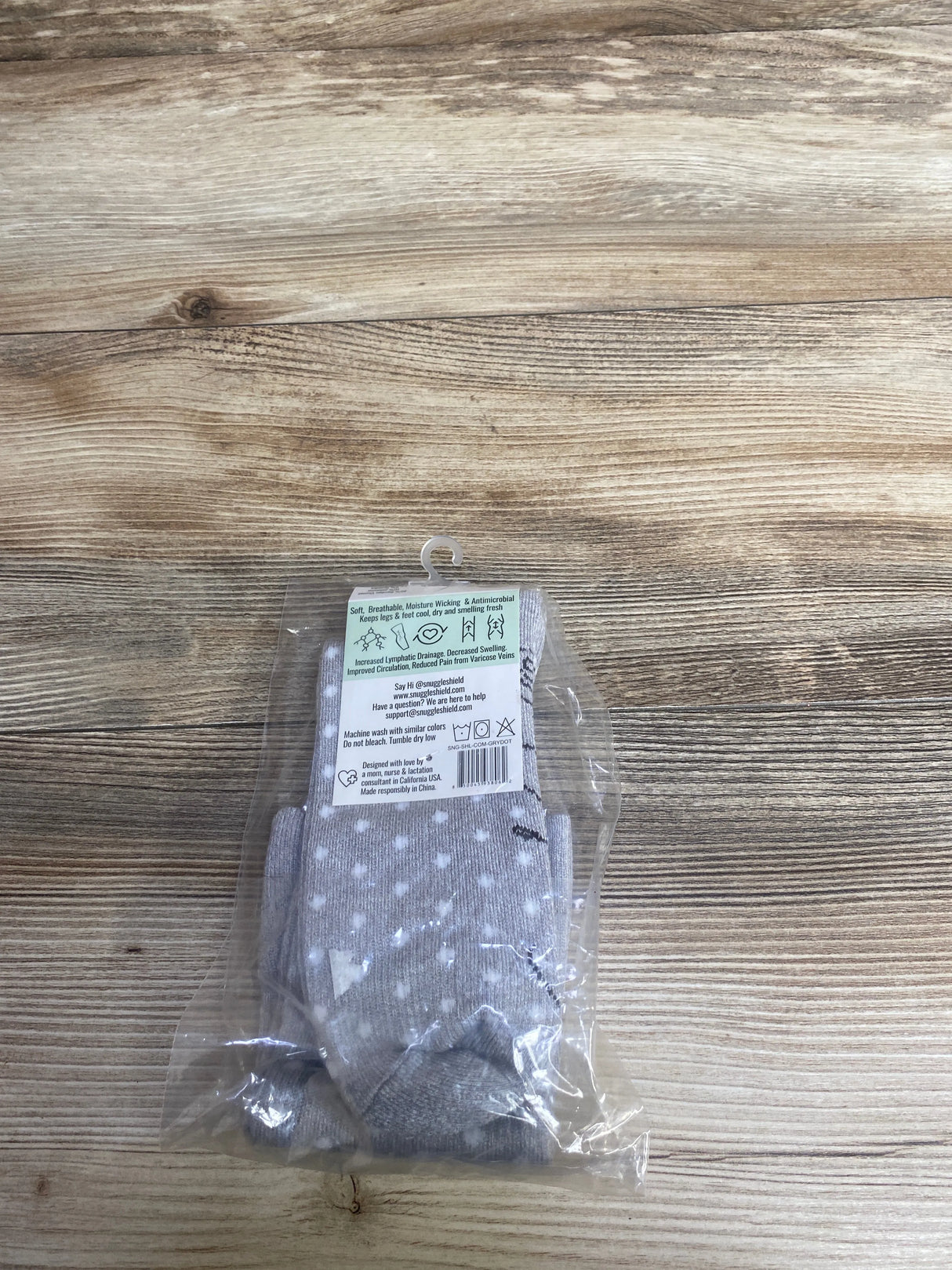 Gray and white polka dot compression socks in packaging on a wooden surface for kids and adults