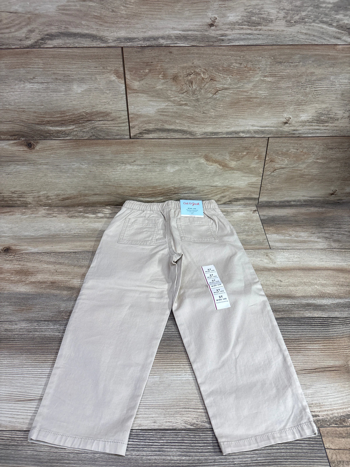 Back view of beige Cat & Jack wide leg drawstring joggers, size 3T, showcasing back pockets with wood plank background