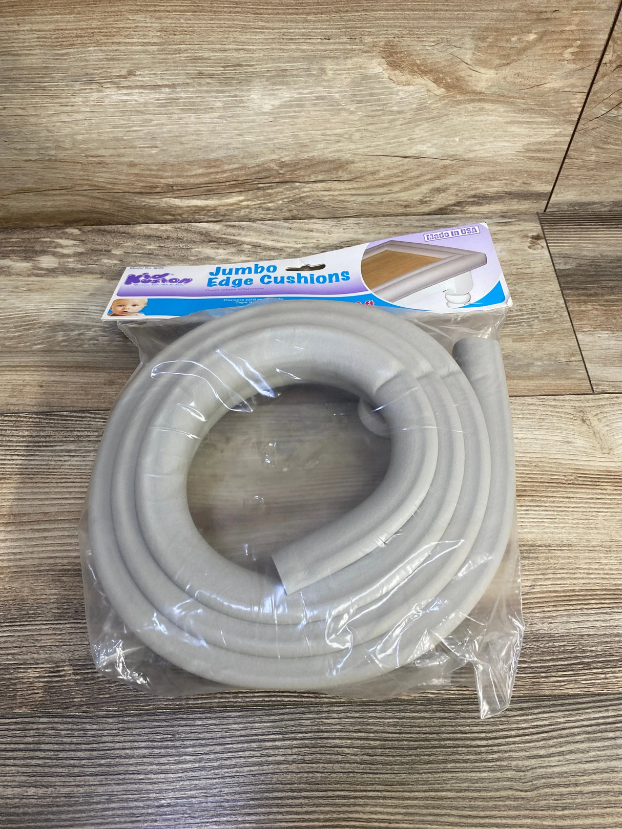 Top-down view of KidKusion jumbo edge cushion in taupe with thick foam padding coiled in plastic packaging on wood floor