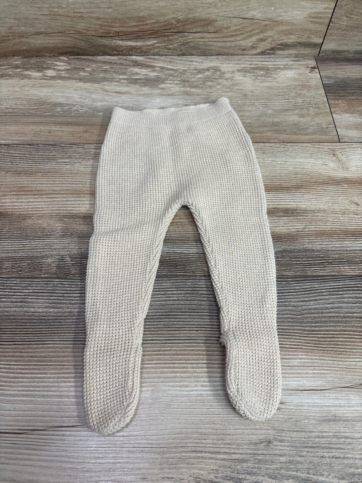 Top view of Zara knit footed pants in beige, size 1-3m, showcasing knitted texture with a wood-grain background