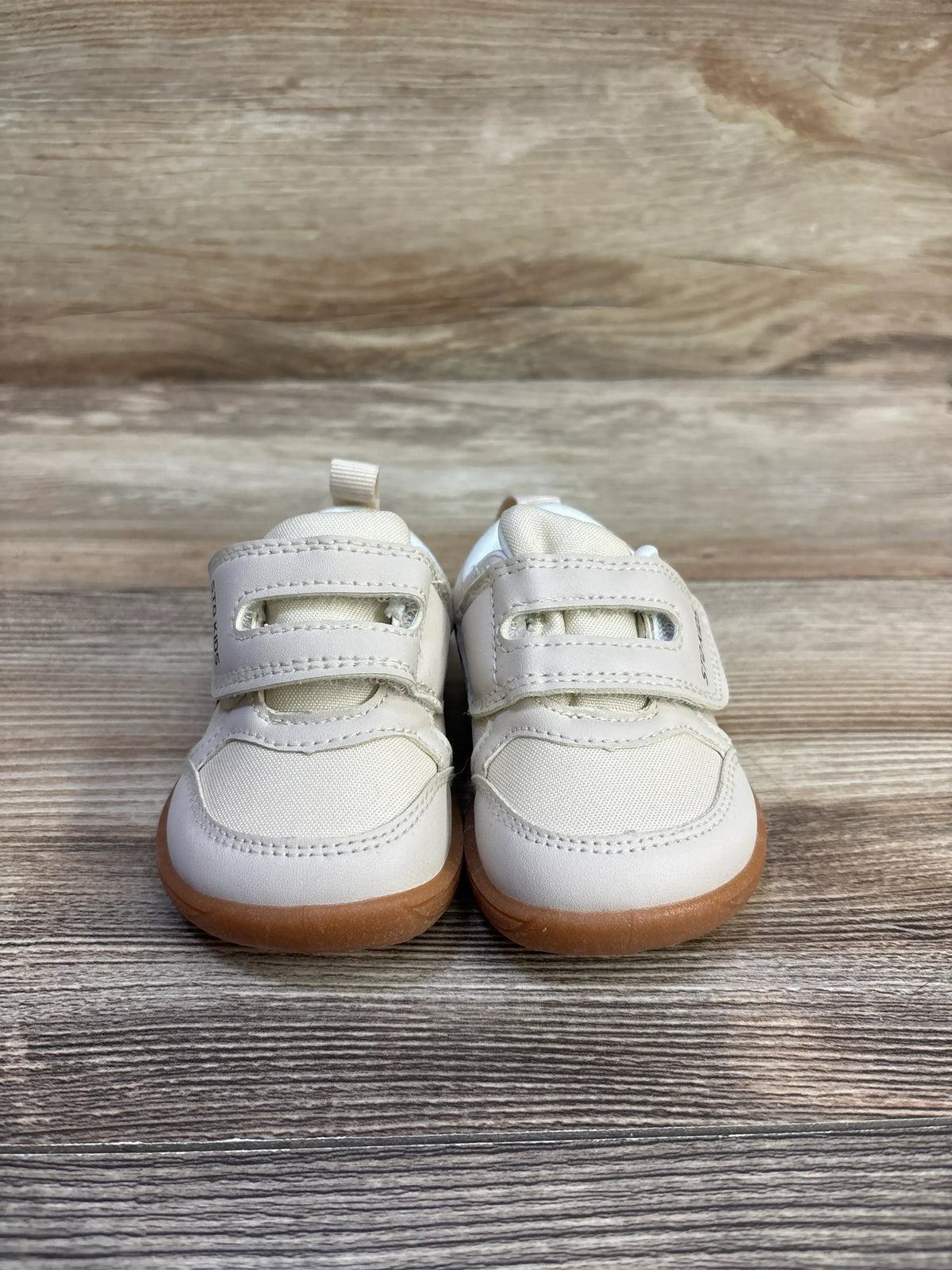 Front view of STQ kids first walking sneakers in tan, showcasing hook-and-loop straps and gum soles on a wood surface