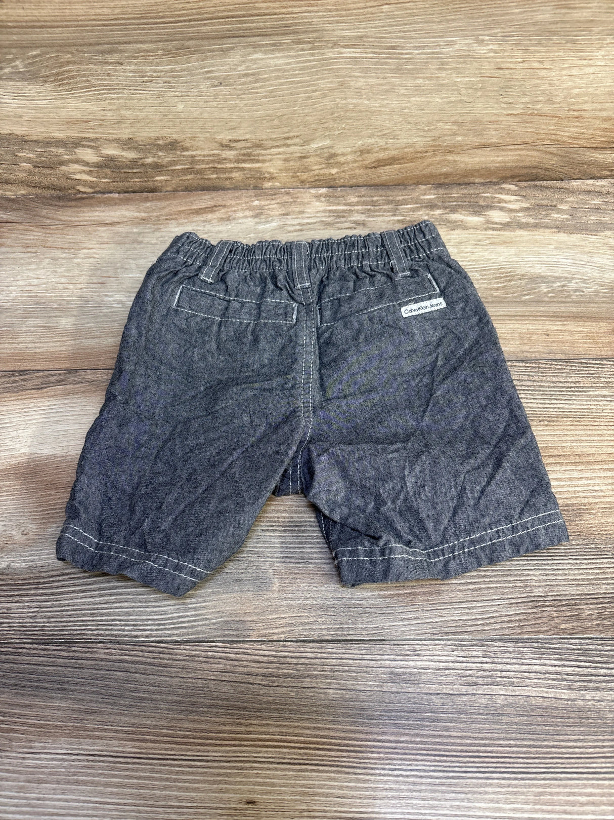 Back view of grey Calvin Klein toddler shorts showcasing elastic waistband and faux back pockets on wood background