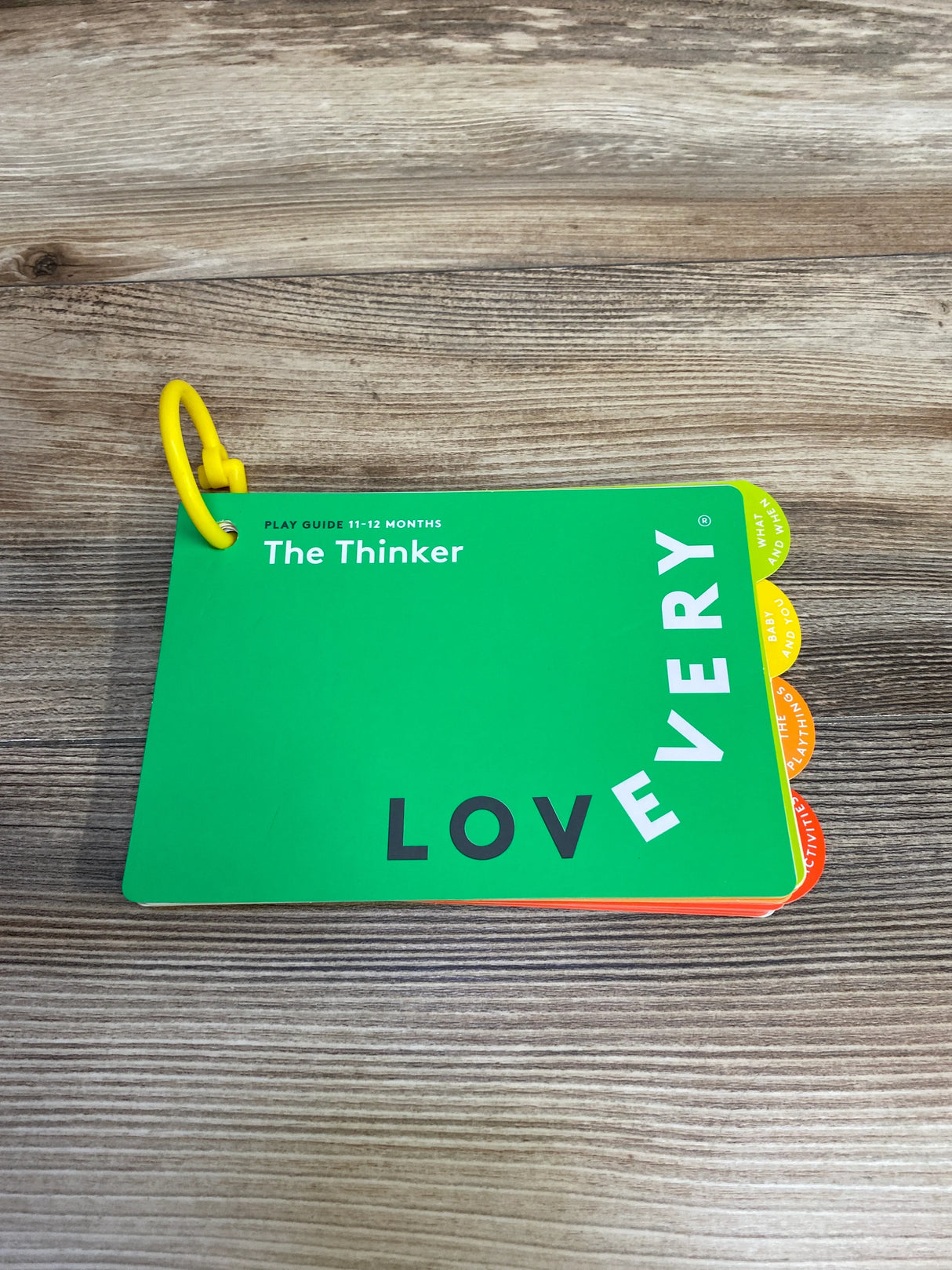 Lovevery play guide booklet for 11-12 months titled The Thinker with colorful tabs on wood surface