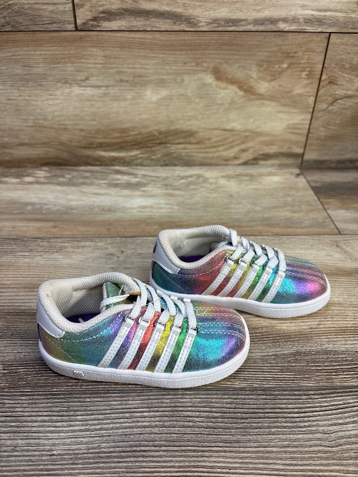 Angled view of K-Swiss Classic VN sneakers showing iridescent rainbow upper, white stripes and laces on wood floor